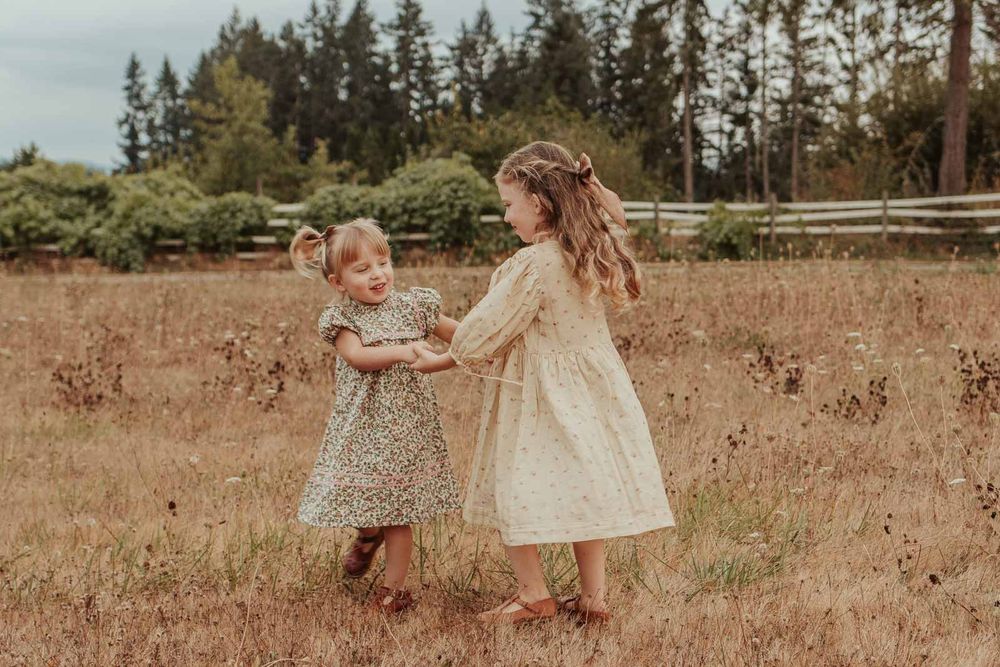two little sisters holding hands and spinning in a grassy field wearing floral dresses and bows