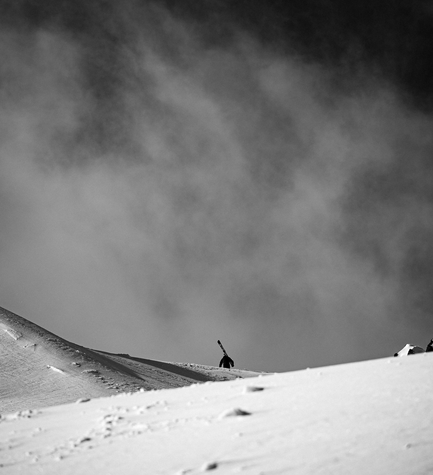 Black and white photograph of lone skier ascending snowy mountain slope in misty conditions.