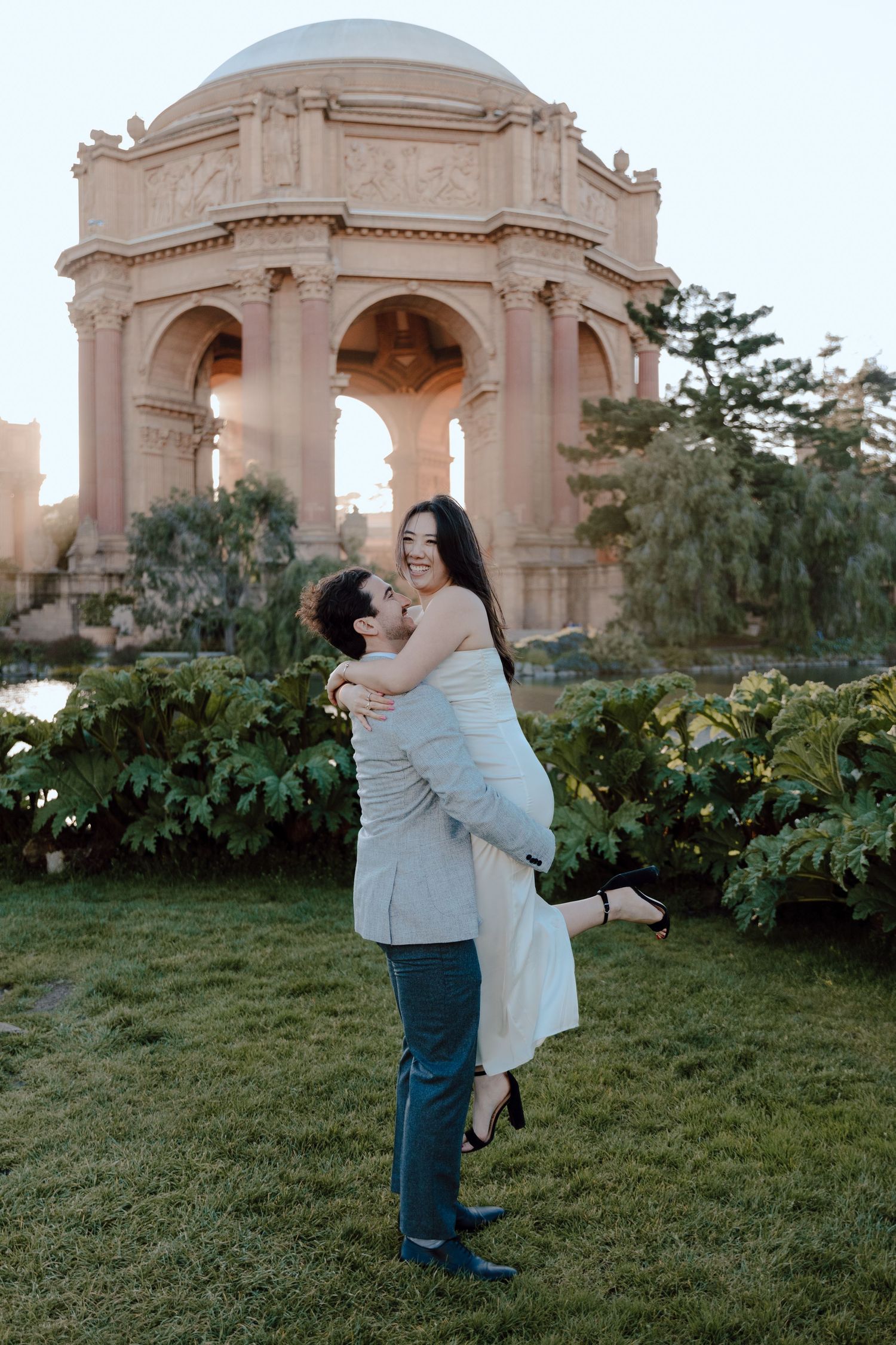 Couple embracing in front of Palace of Fine Arts dome in San Francisco at sunset.