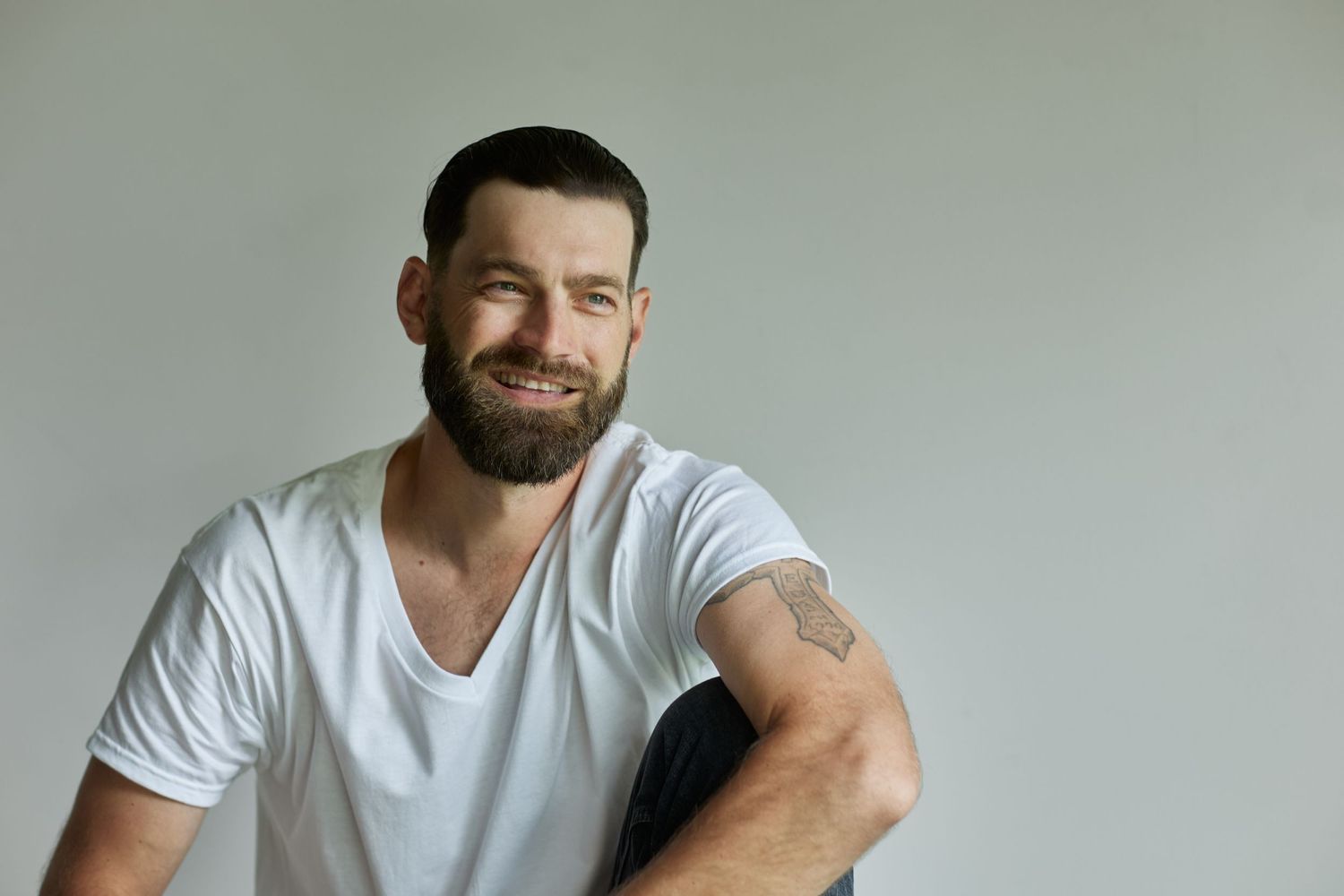 Casual portrait in white v-neck t-shirt showing relaxed pose against light background.