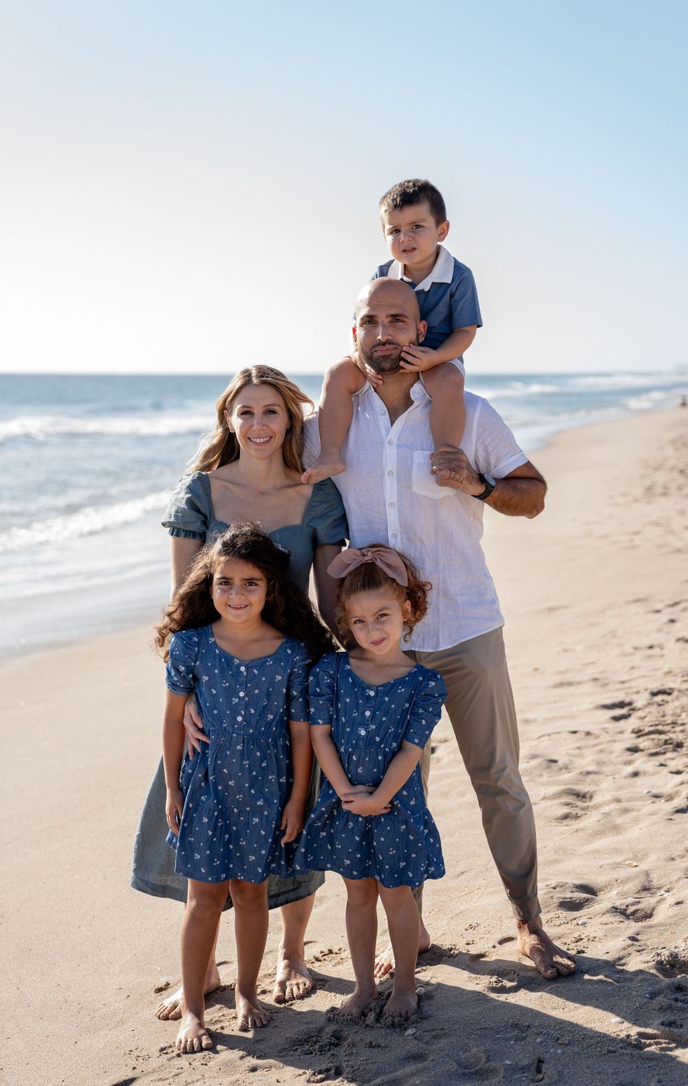 Family walking and playing together on sunny beach with ocean waves in background.