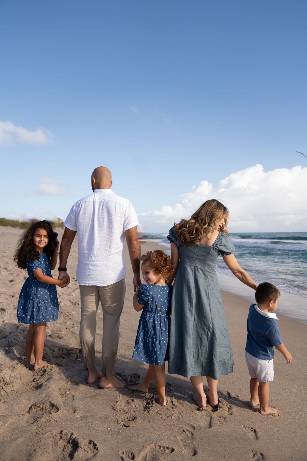 Family holding hands while walking along the shoreline on a beautiful beach day.