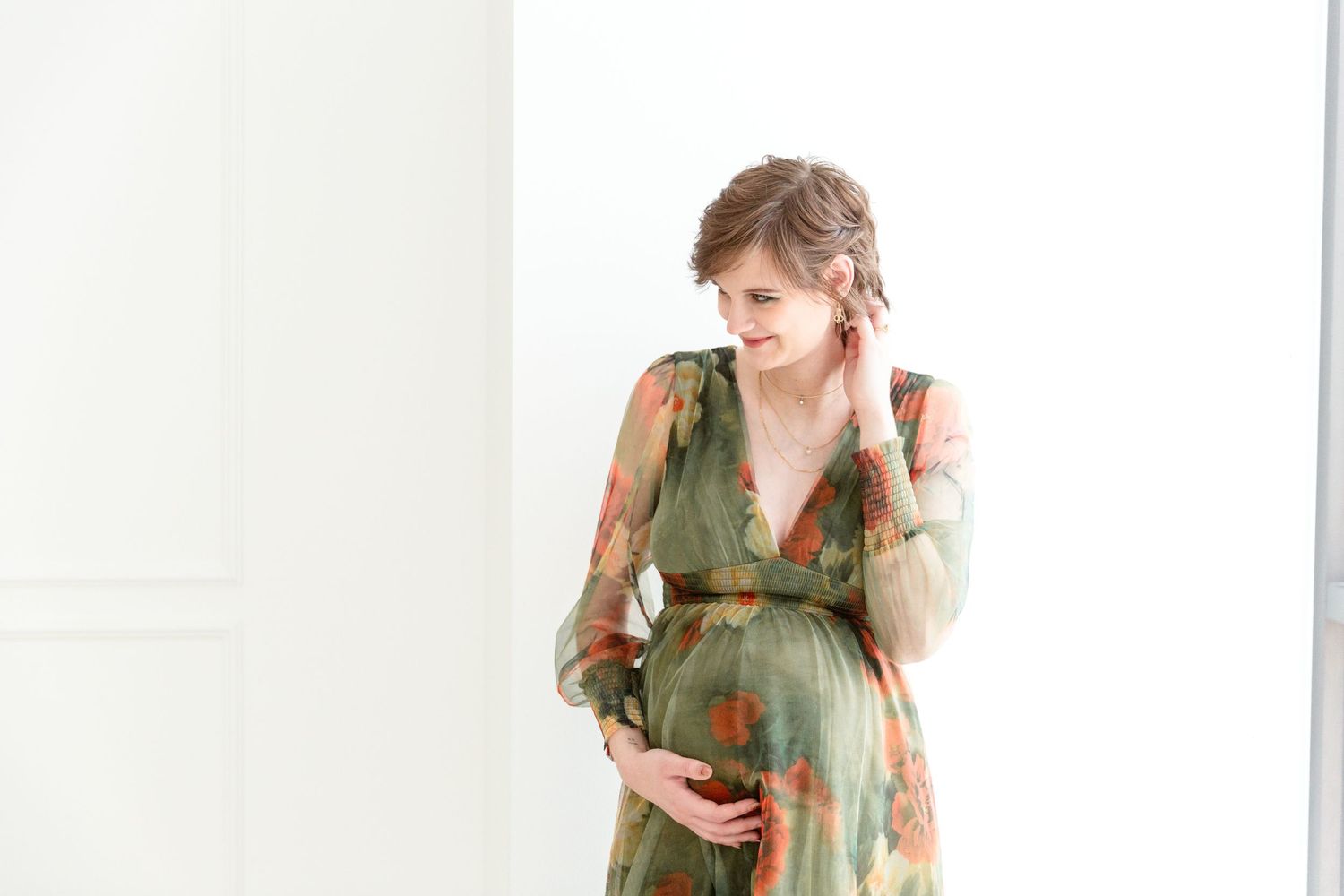 Maternity picture of woman in green floral dress against white background in studio.