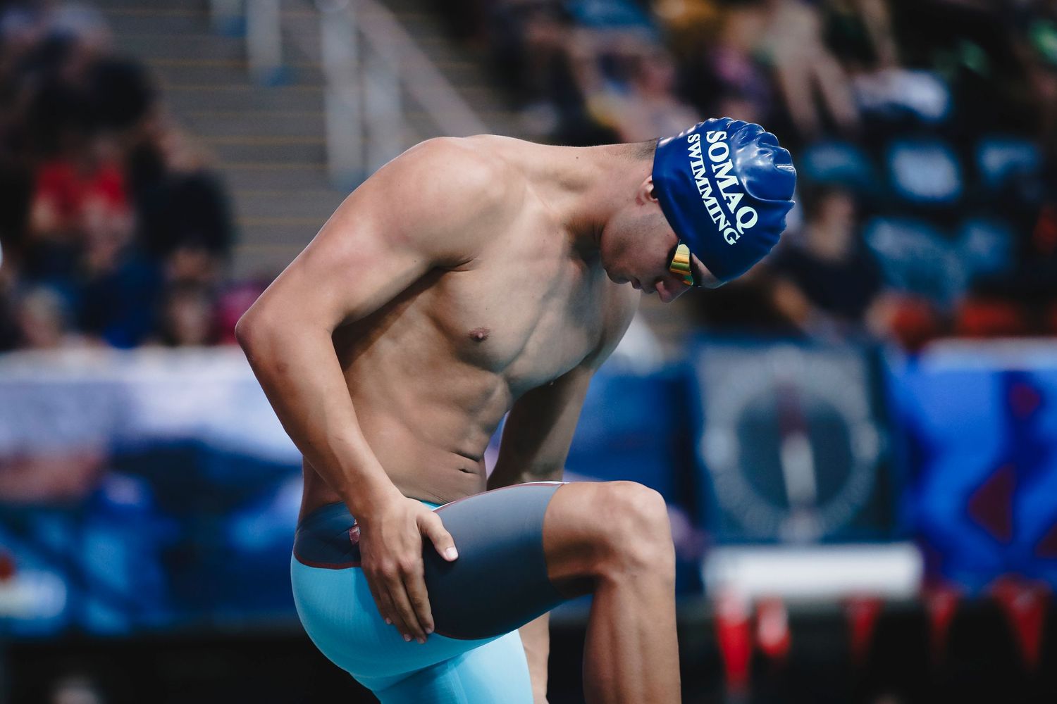 Competitive swimmer on starting block preparing to dive into pool.