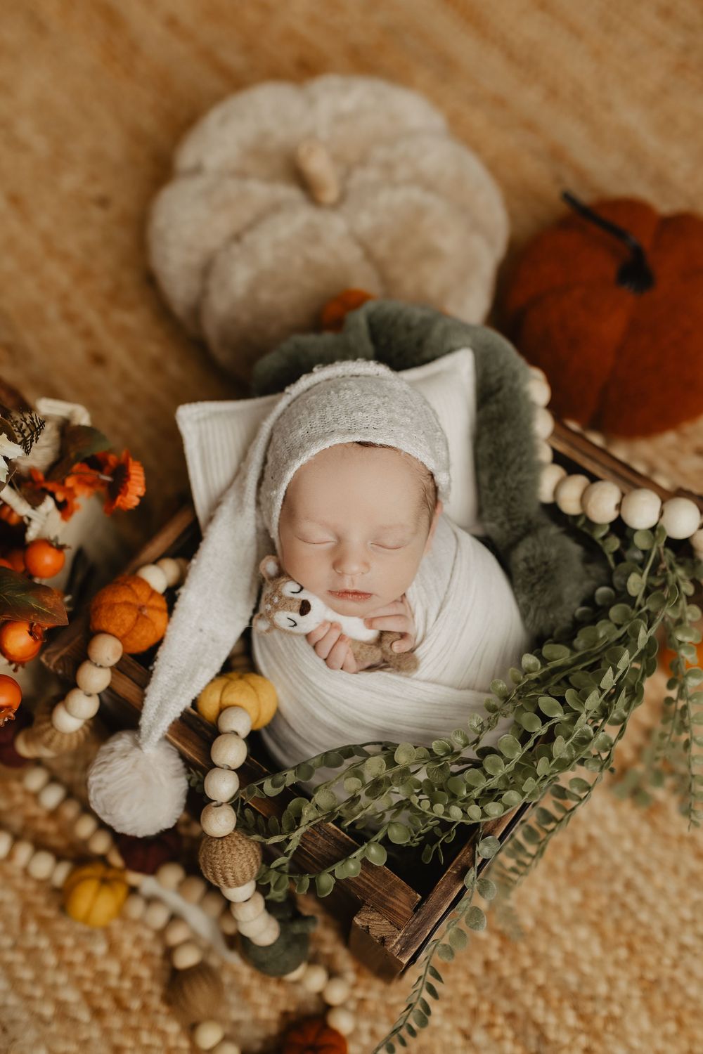 Fall themed newborn setup with pumpkins, wooden beads, and eucalyptus on textured surface.