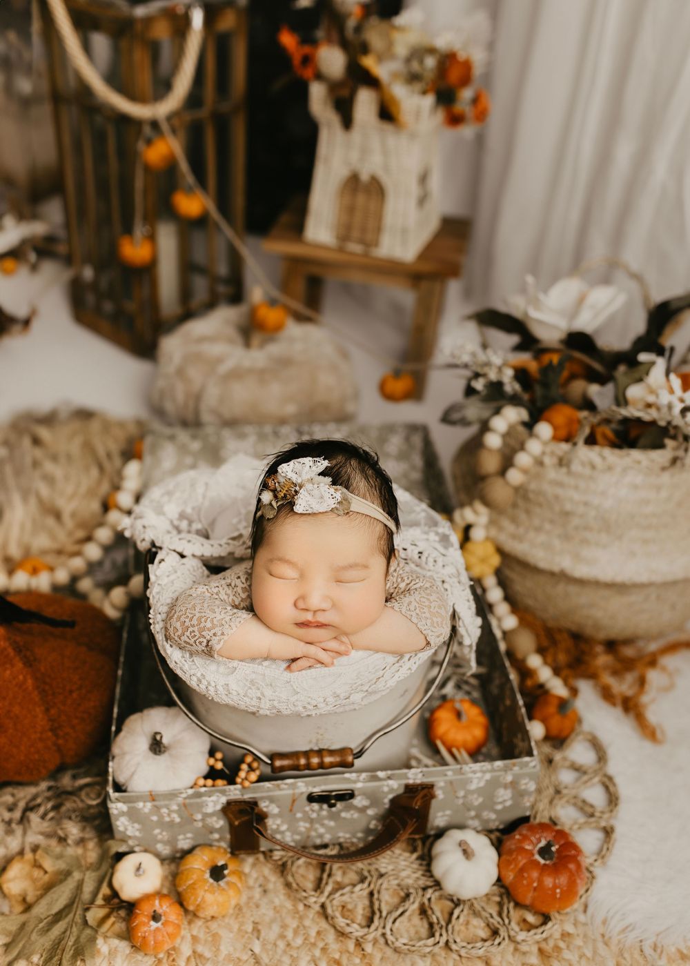 Newborn photography with autumn theme featuring white pumpkins and lace decorations.