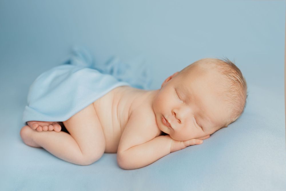 Sleeping baby lying on light blue backdrop in minimalist newborn photography setting.