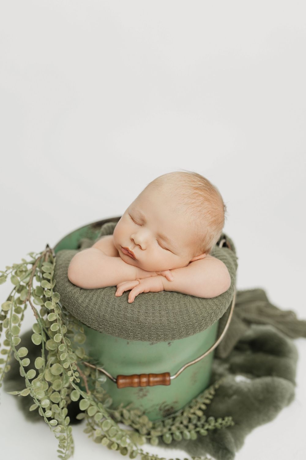 Newborn sleeping on vintage green hat box surrounded by delicate foliage.