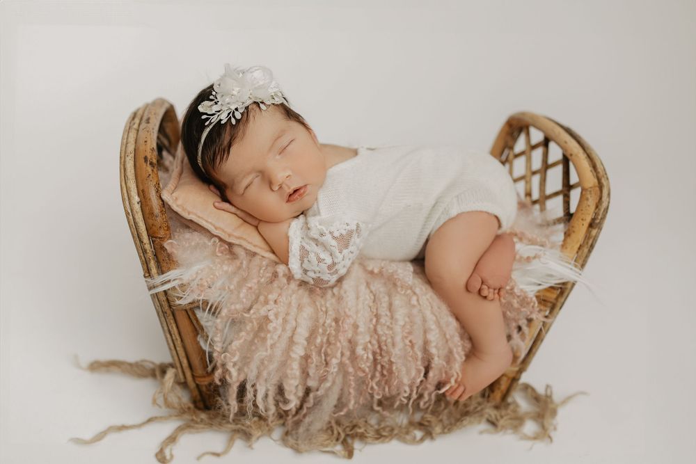 Sleeping baby in lace dress resting in vintage wicker chair.