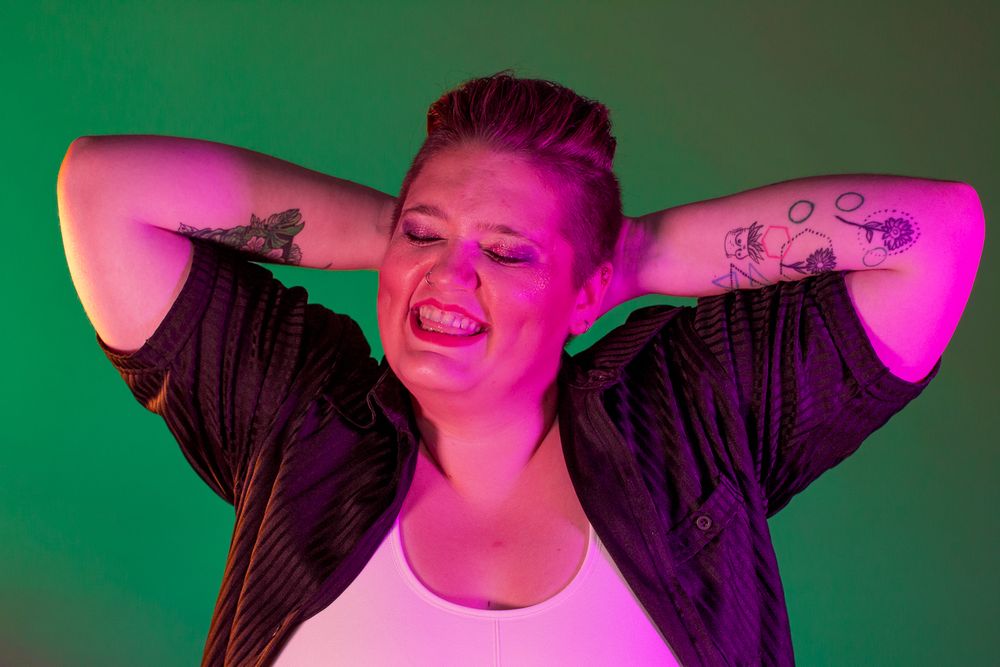 Creative portrait with pink and green lighting against dark background showing joyful expression.