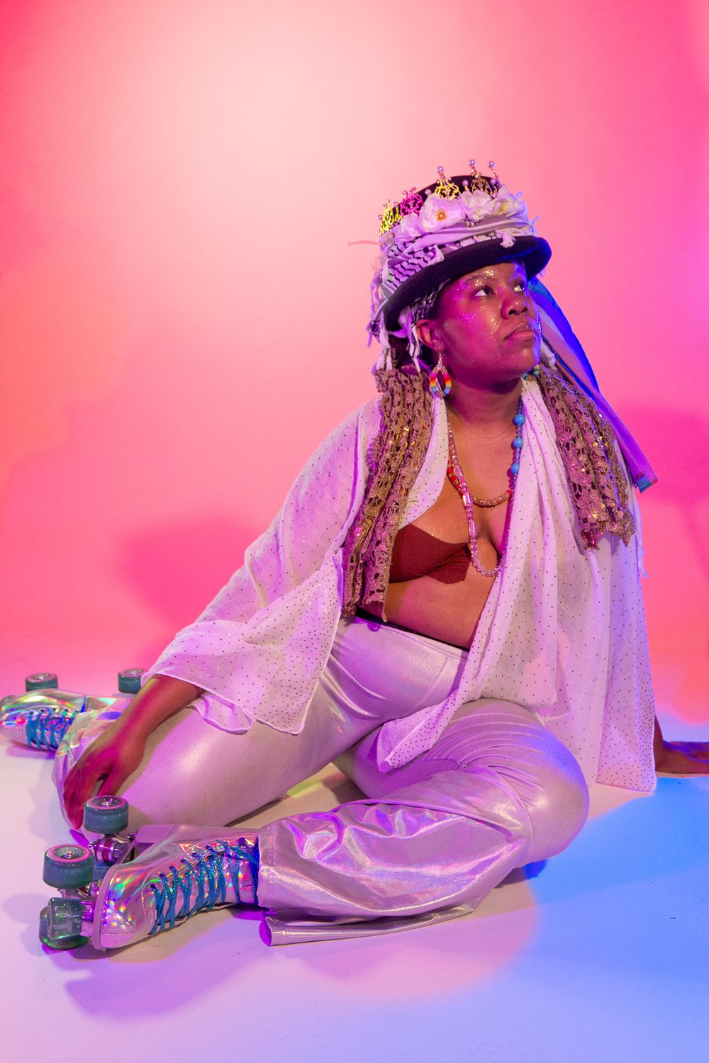 Person in white ensemble with decorated hat posing on floor with roller skates.