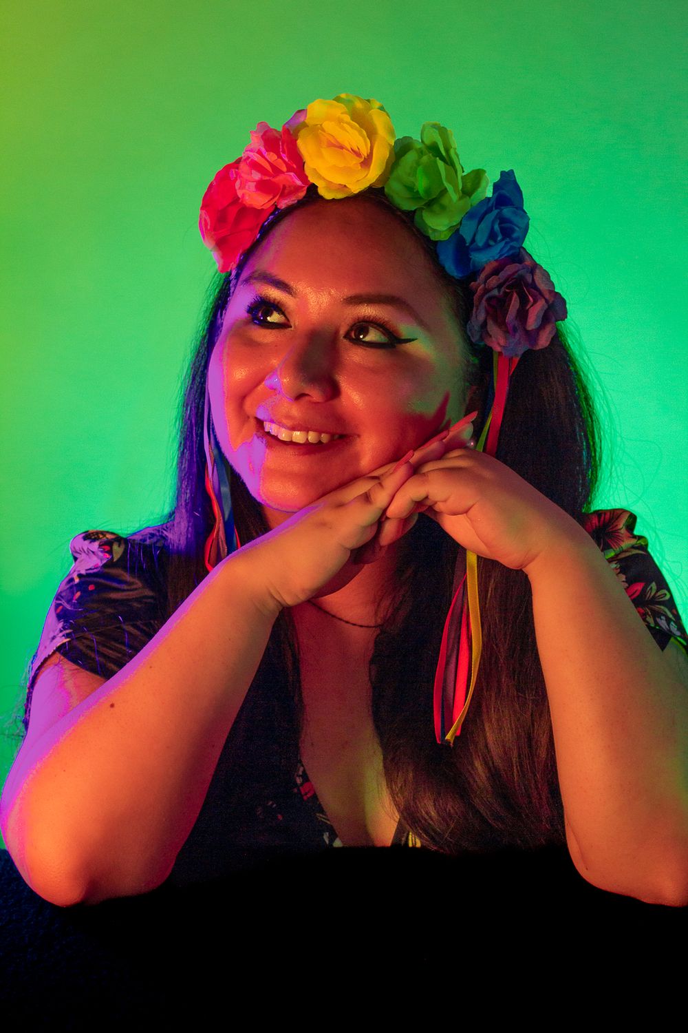 Portrait with rainbow flower crown against green lighting creating a magical effect.