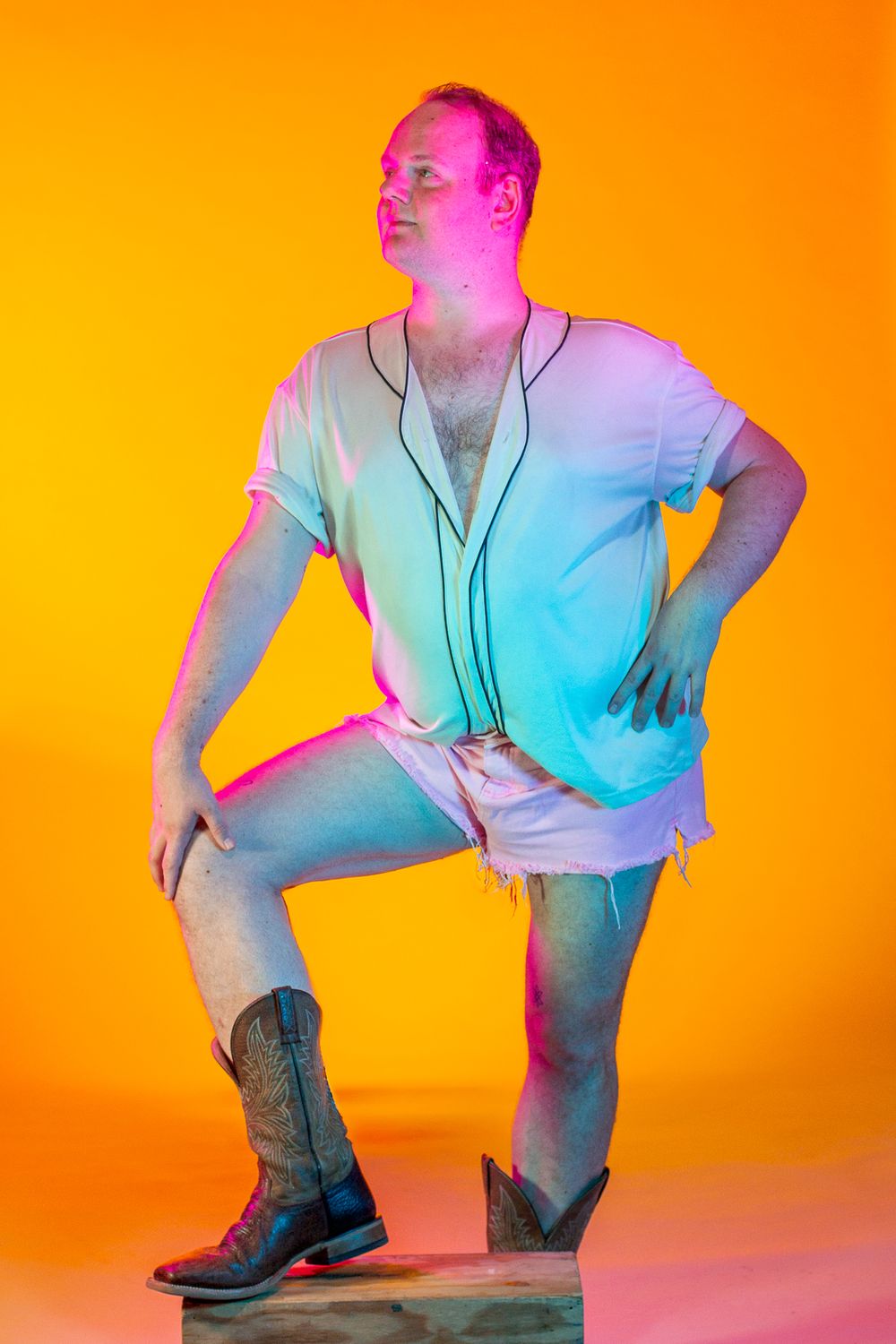 Person in casual attire and boots posing dramatically against orange gradient background.