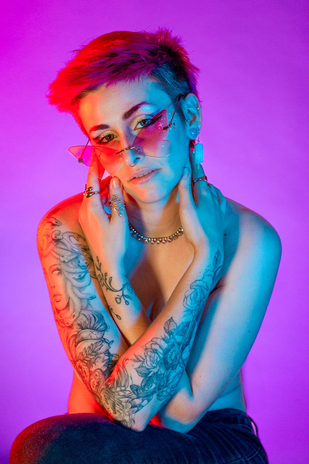 Artistic portrait with dramatic blue and pink lighting highlighting tattoo sleeve and punk rock styling.