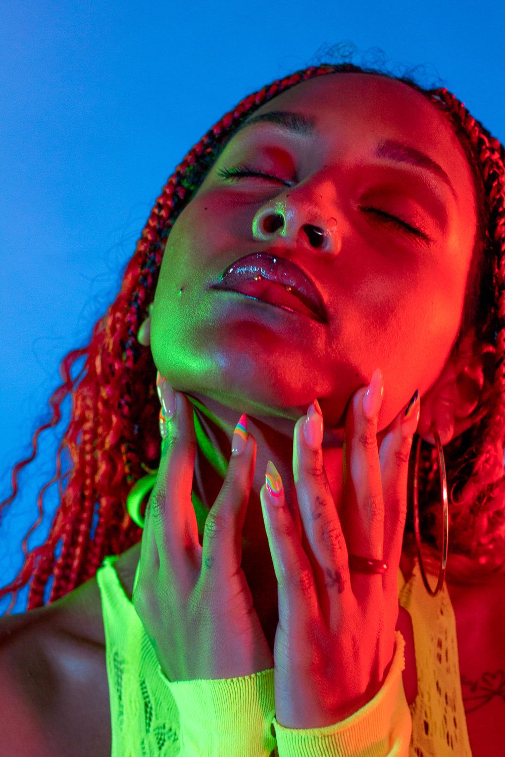Artistic portrait with vibrant red and green lighting showcasing dramatic makeup and braided hair.
