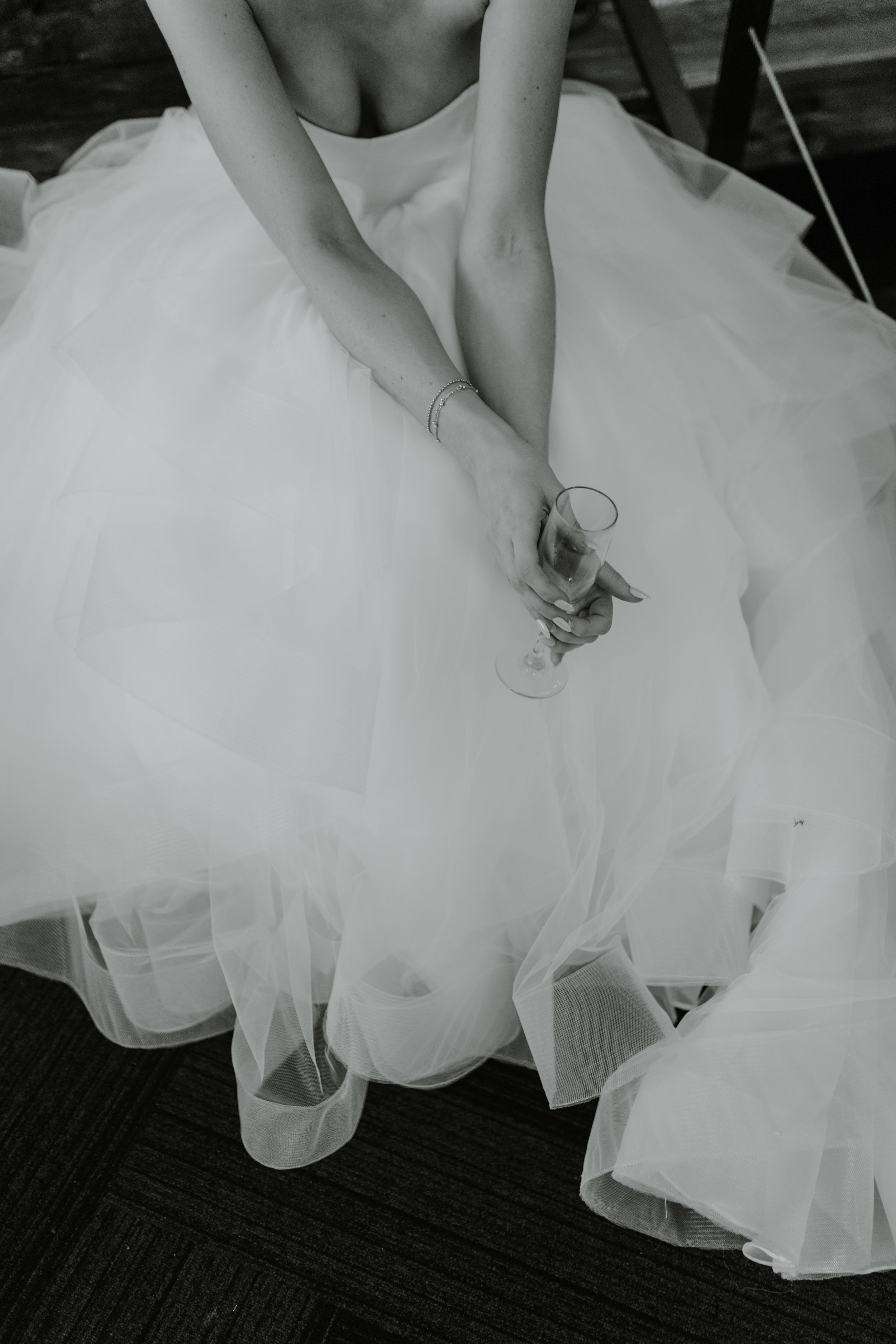 Black and white detail shot of bride's hands and flowing tulle dress against dark flooring.