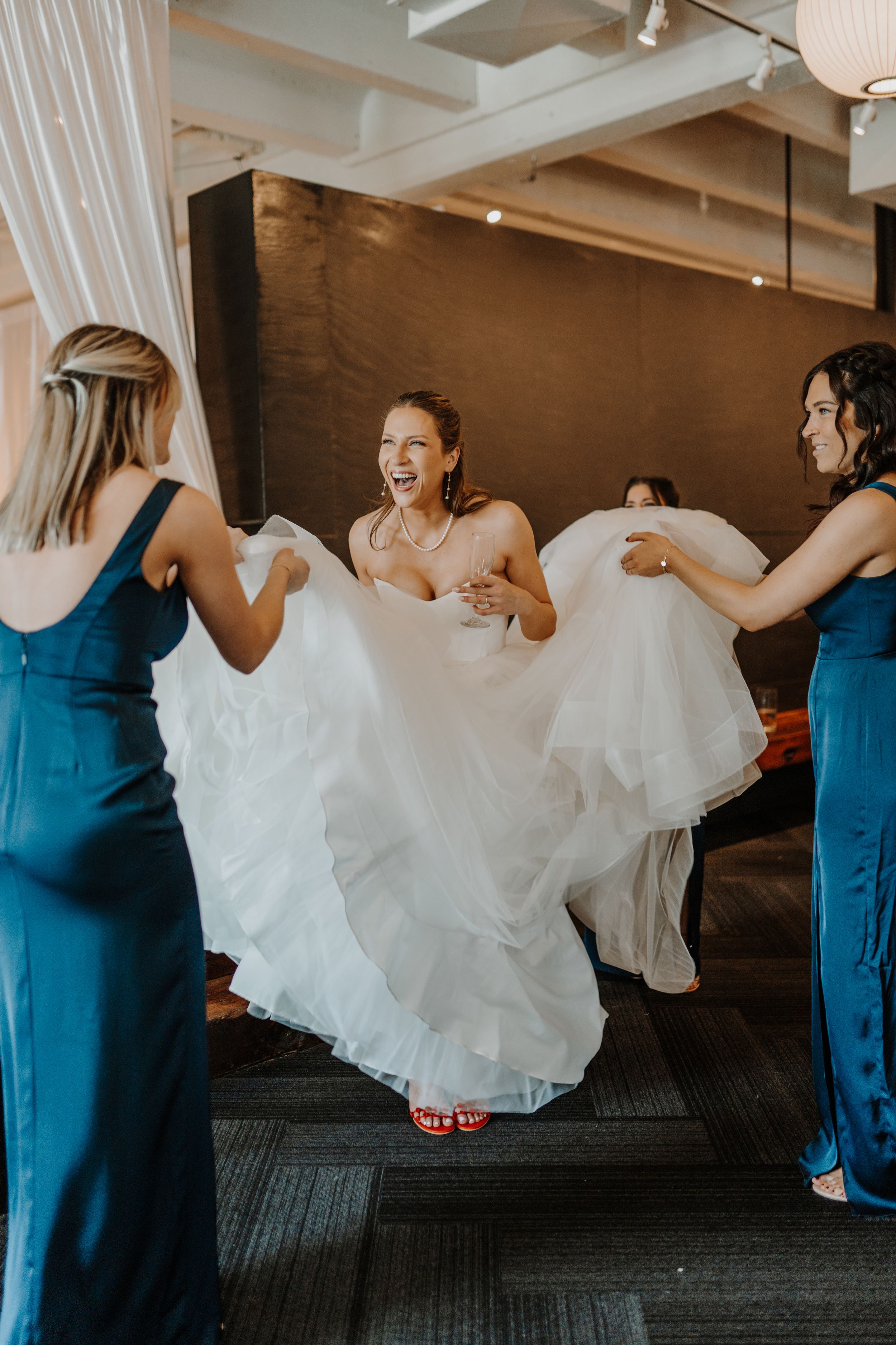 Bridesmaids in blue dresses help bride with her flowing white wedding gown.