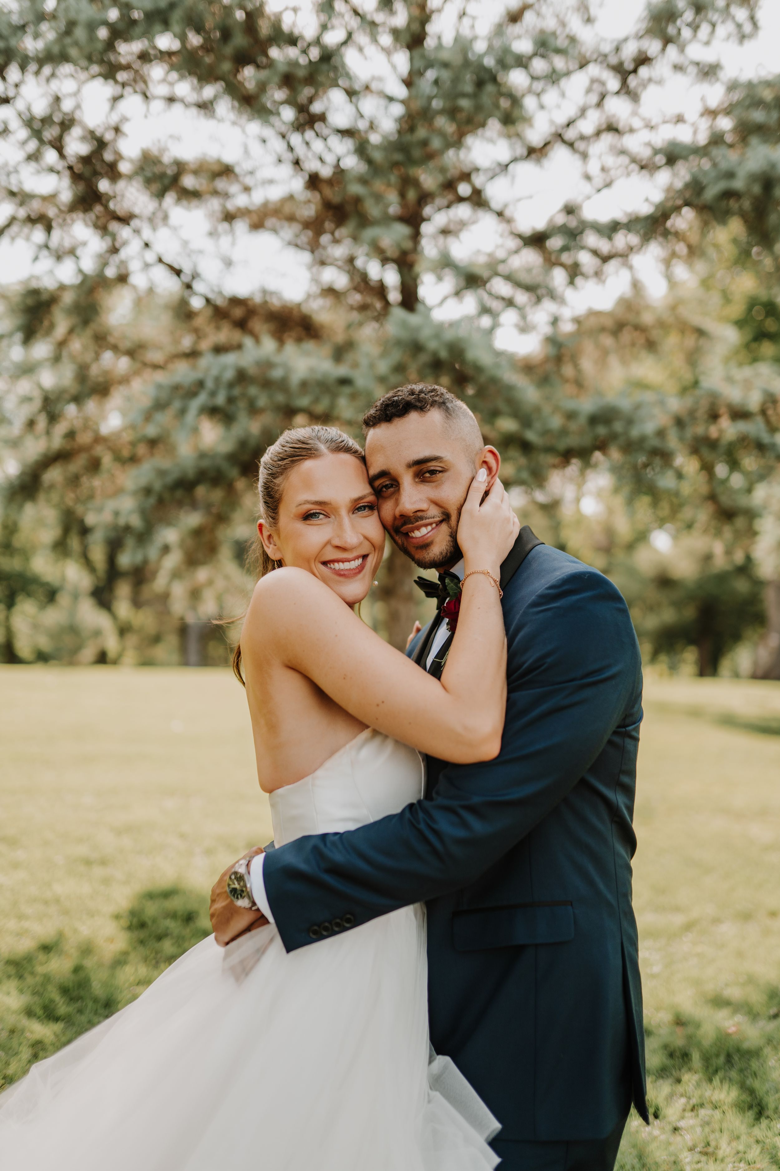 Joyful couple embraces in sunlit garden setting during wedding portraits.