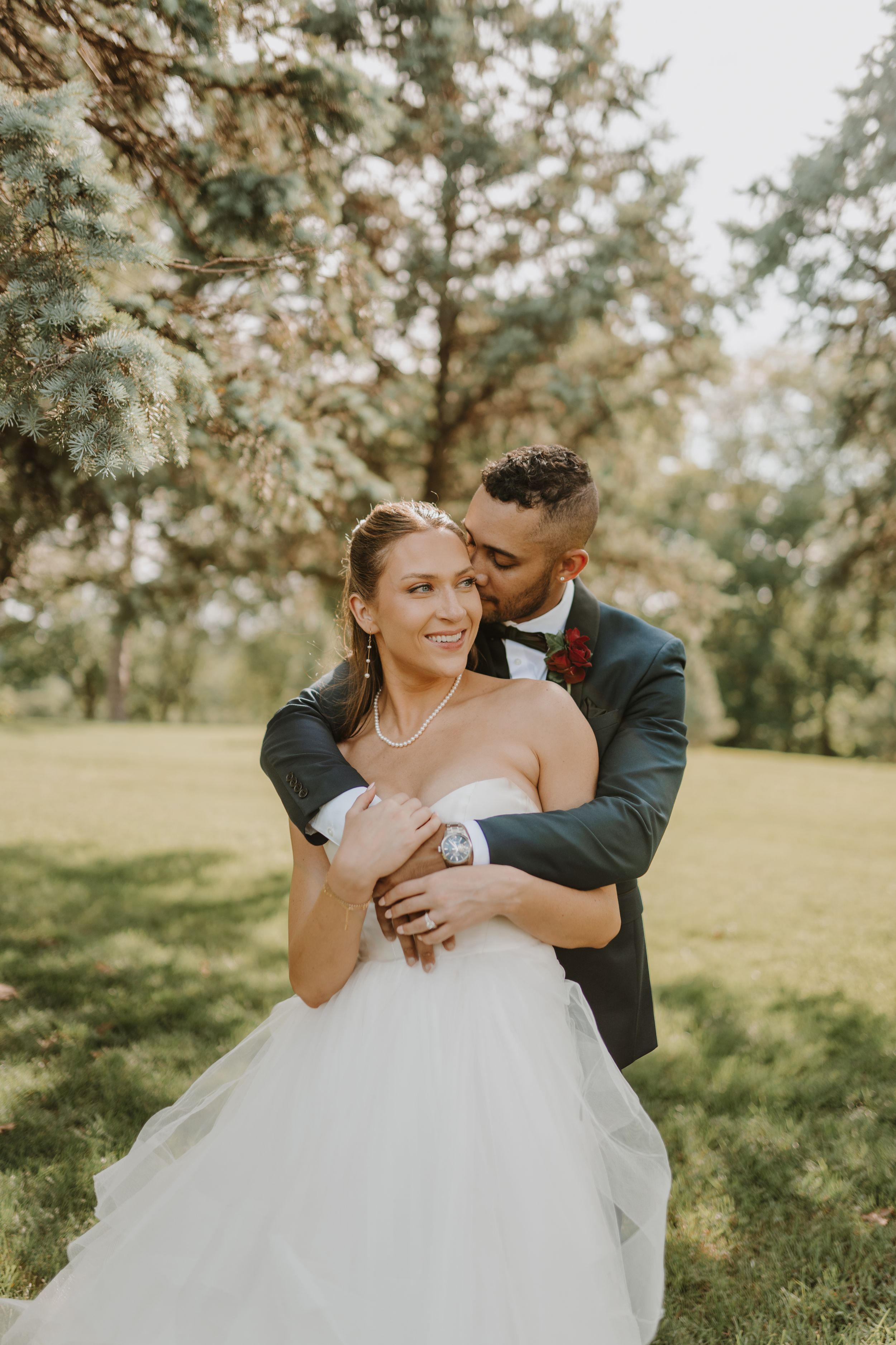 Tender embrace between bride and groom in natural outdoor setting.