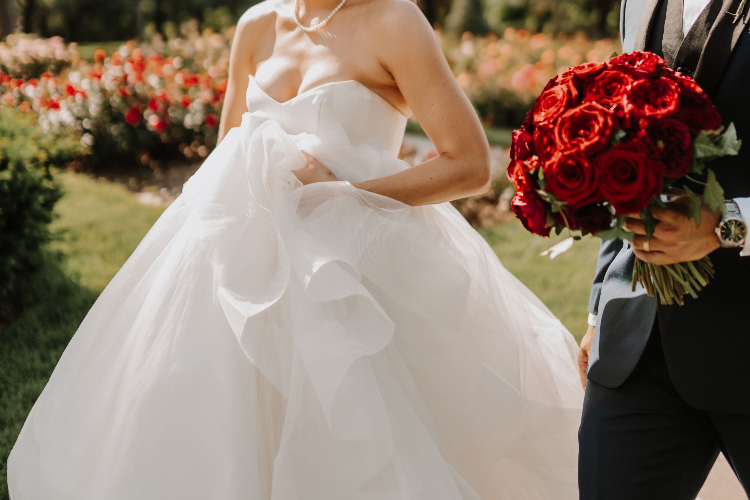 Close-up of bride's white ballgown dress with red rose bouquet visible.