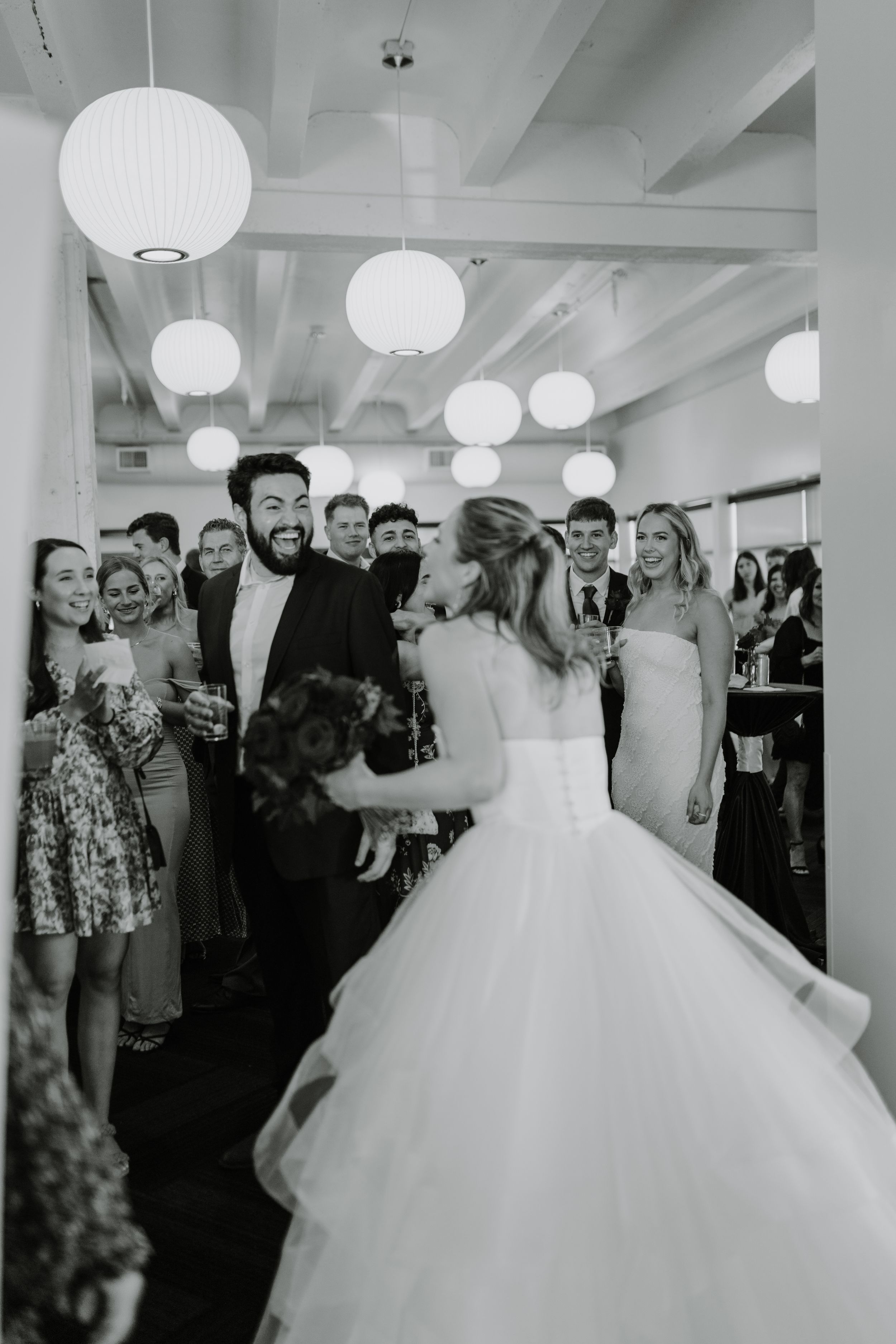 A crowd gathers at an indoor wedding reception with white paper lanterns hanging from the ceiling.