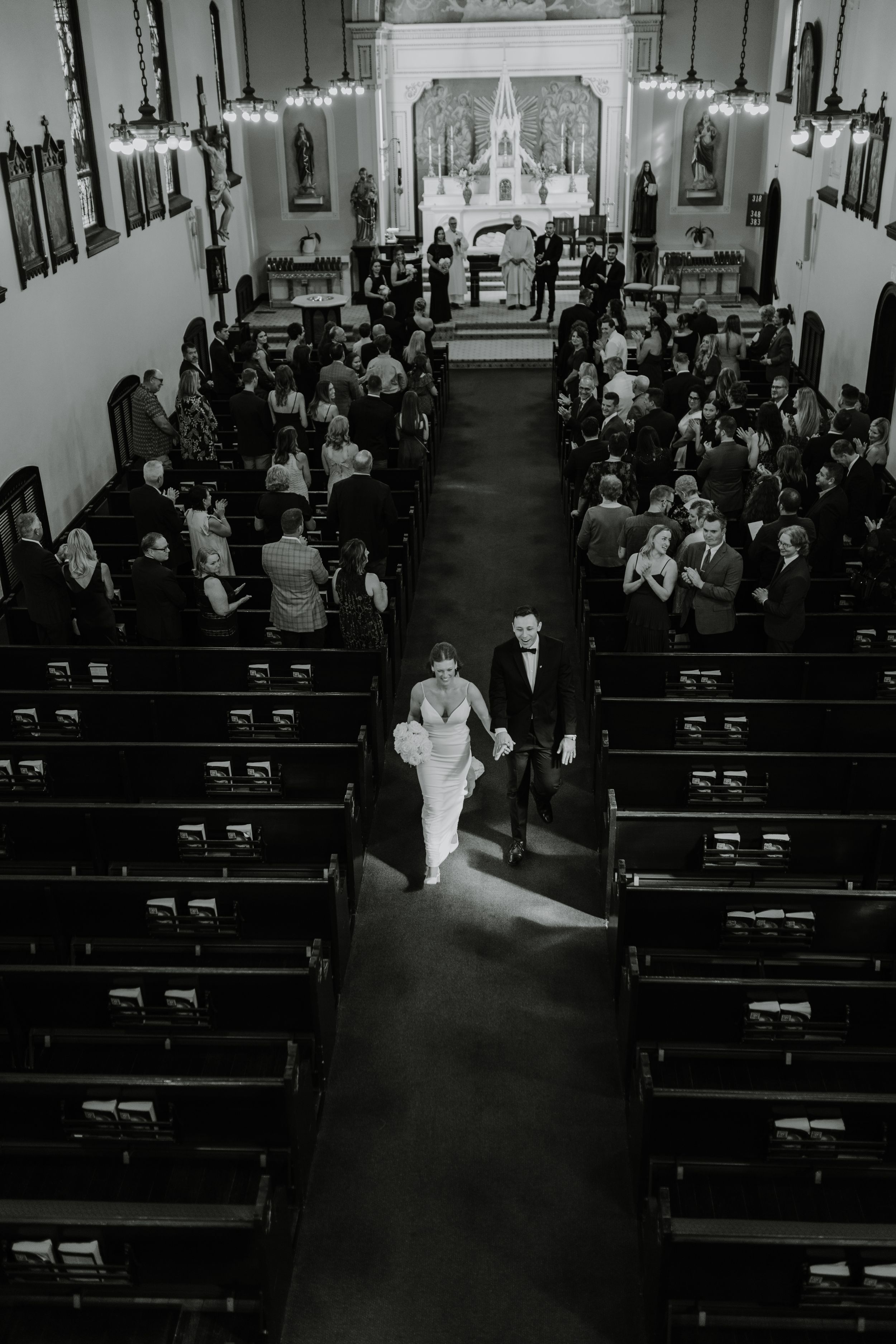 Aerial view of wedding ceremony in traditional church with guests seated in pews.