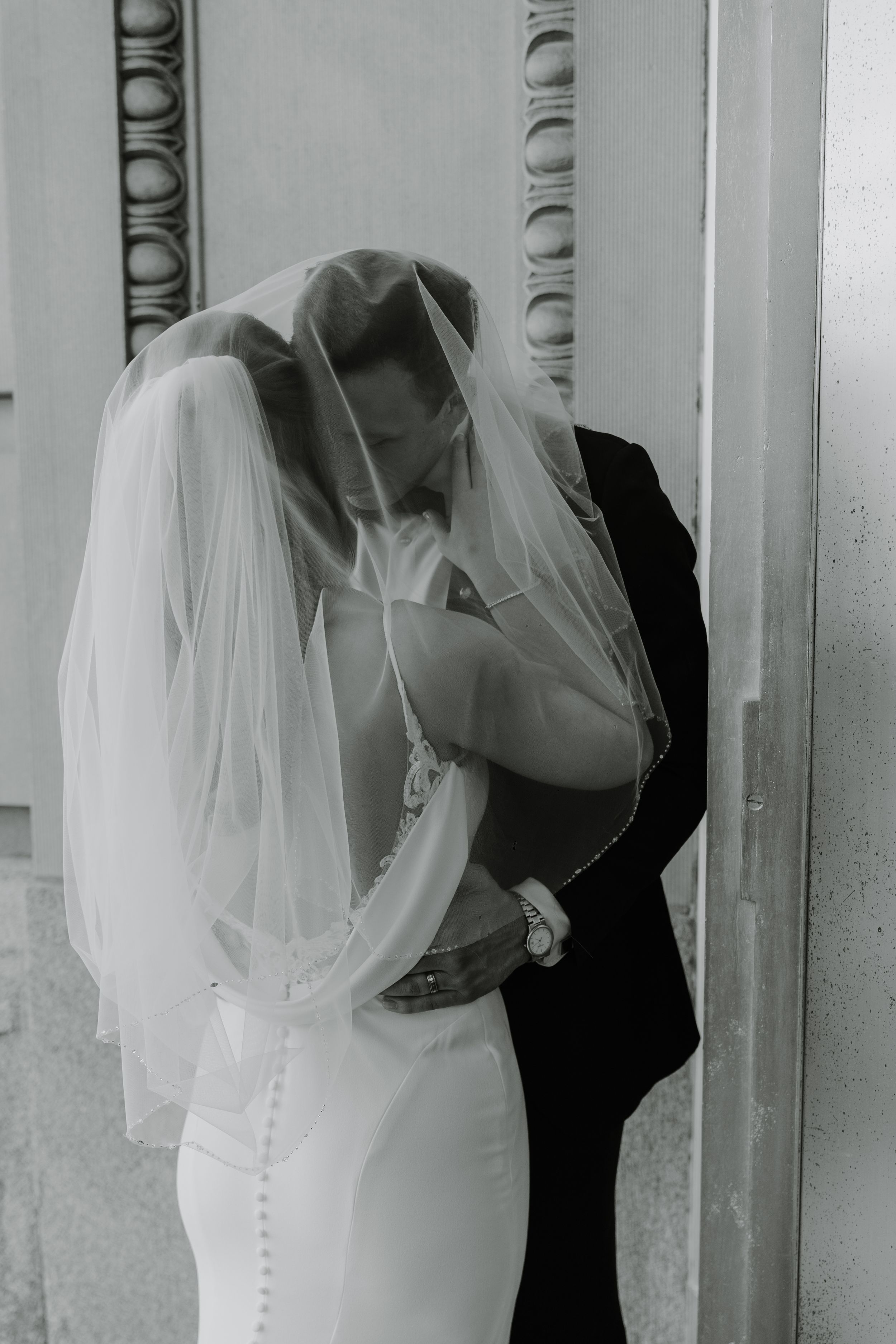 Intimate black and white portrait of couple embracing under bride's veil.