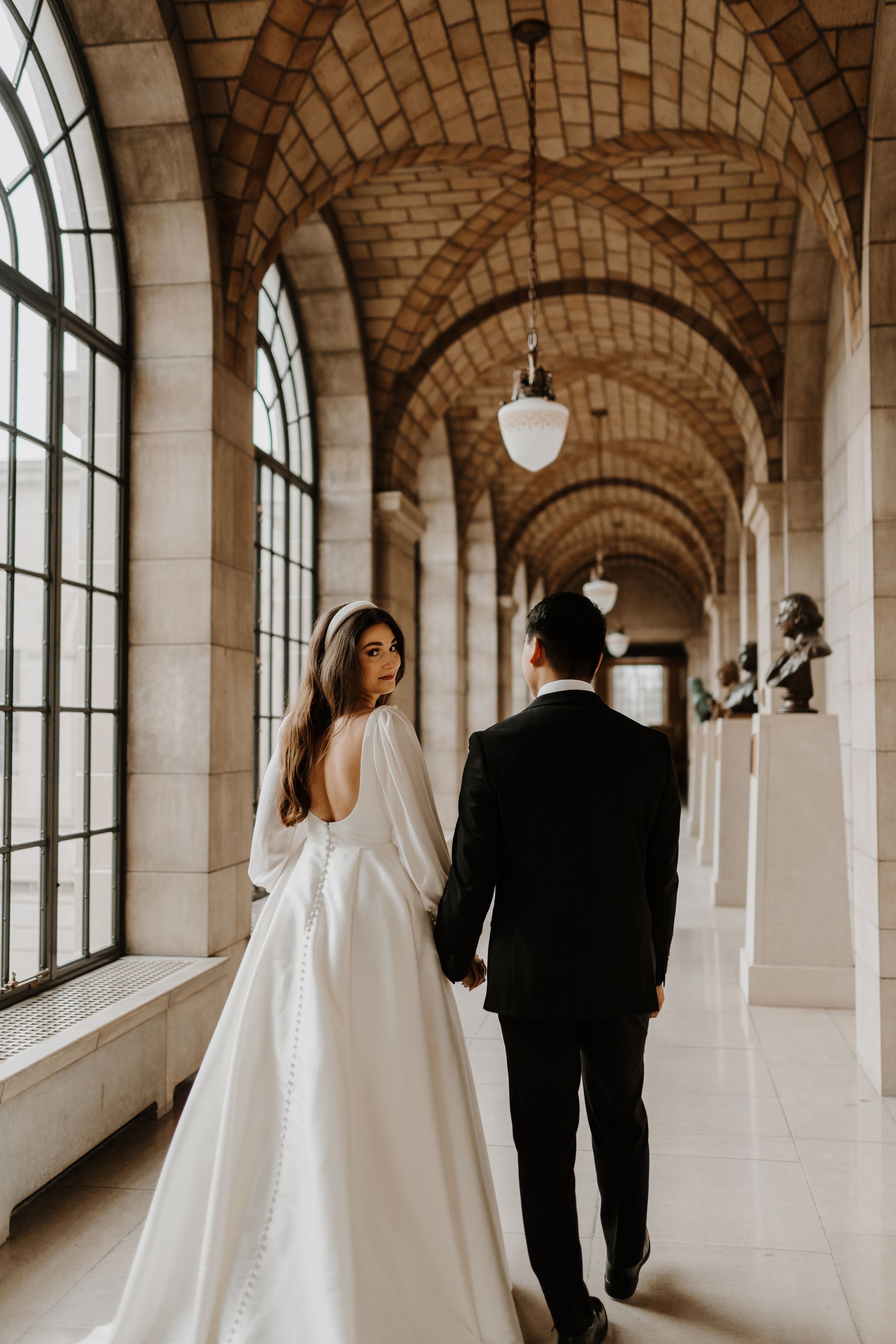 Elegant wedding photos in historic hallway with arched windows and stone architecture.