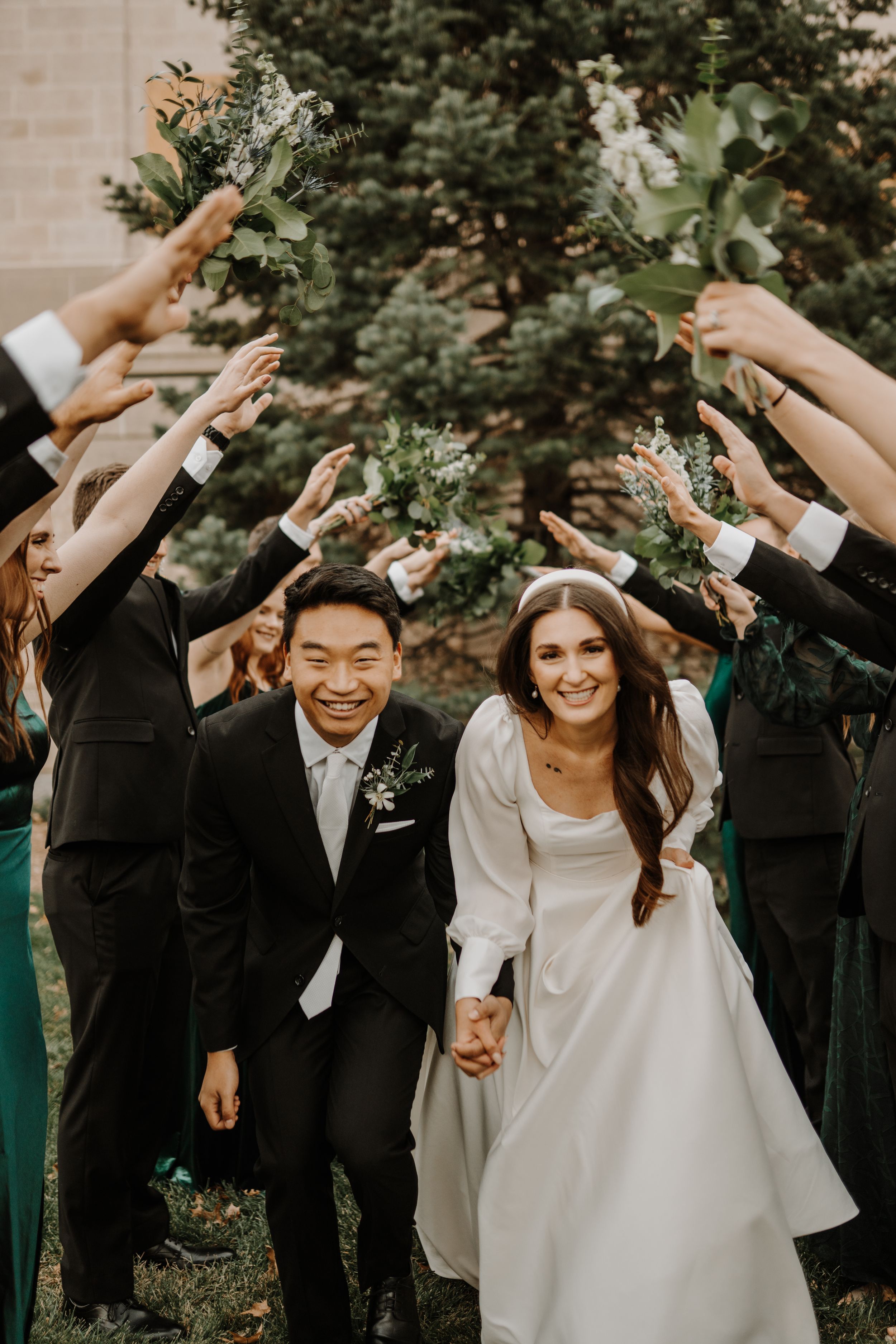 Joyful wedding party celebrating with raised arms in outdoor garden setting.