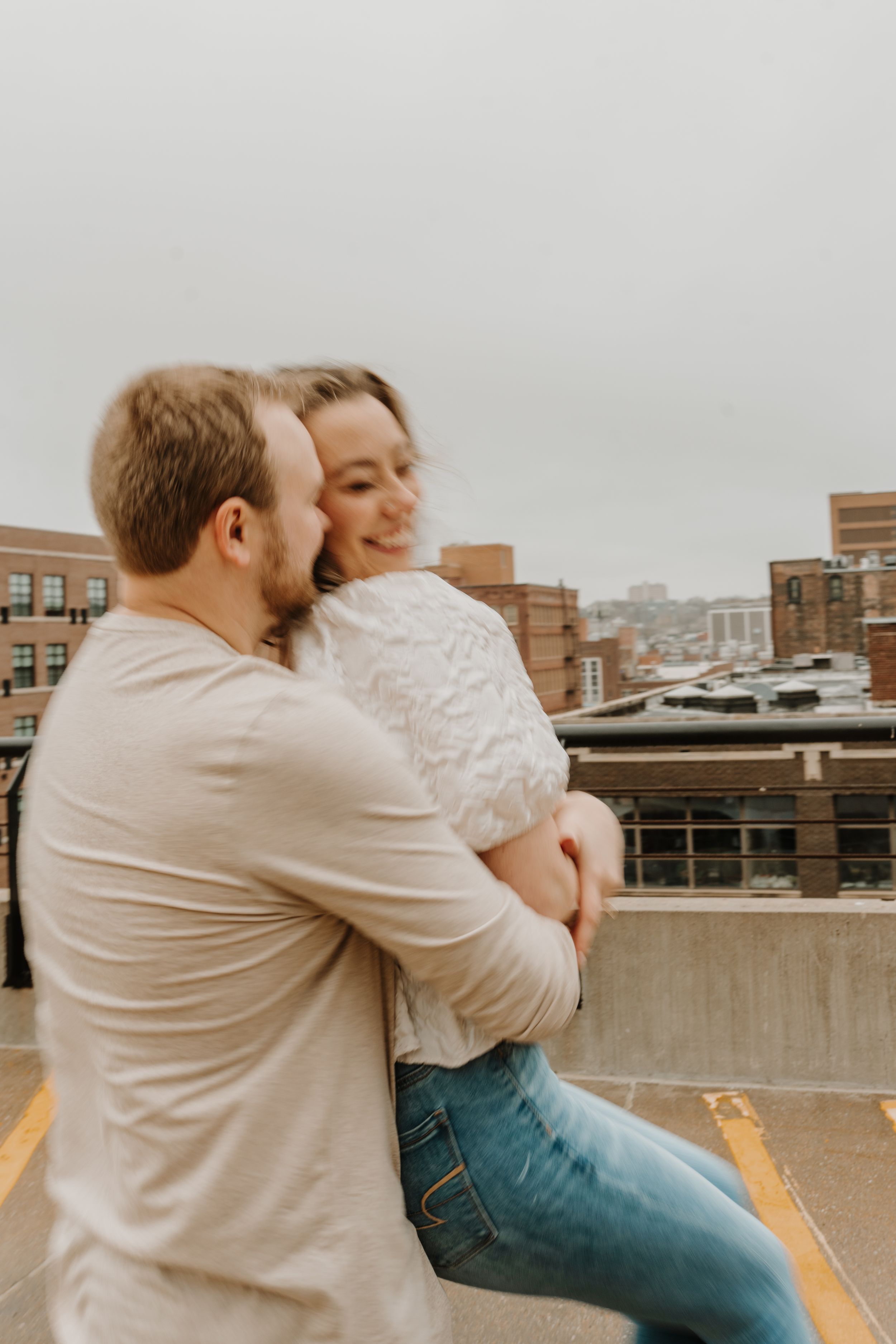 Couple in jeans and beige embracing and laughing together on city rooftop.