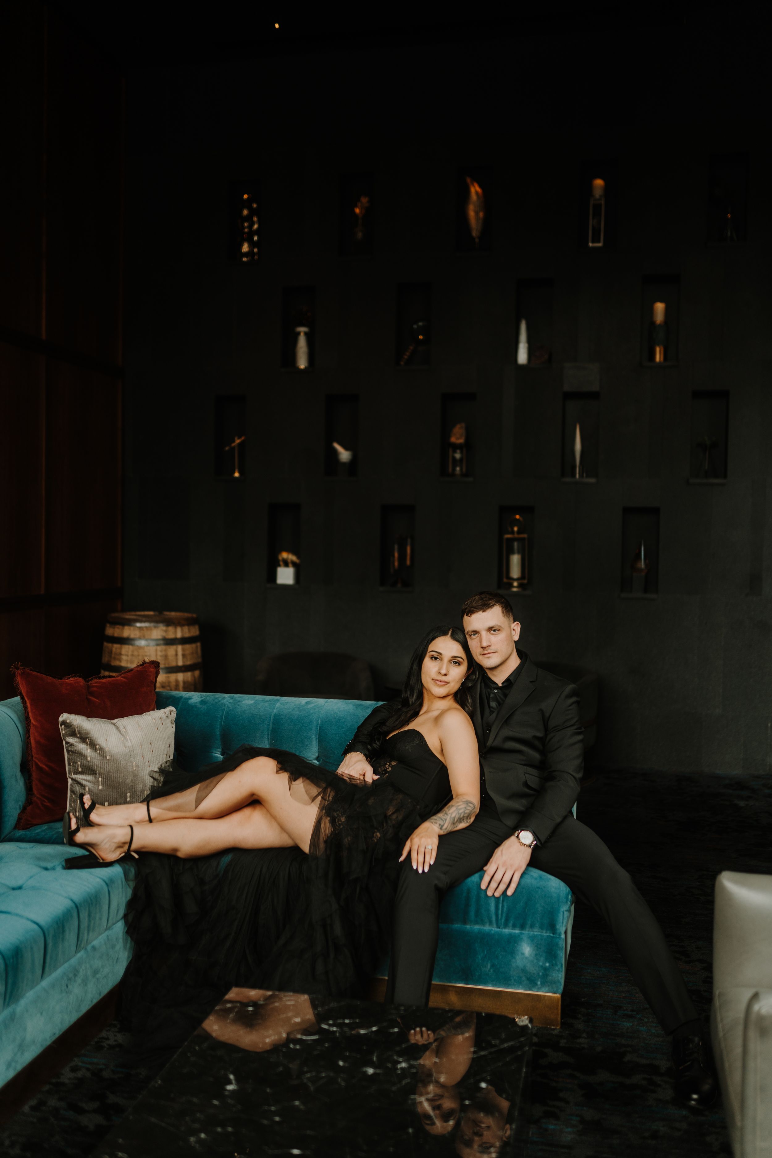 A moody photo series of a couple posing on a blue velvet couch in a dimly lit room.