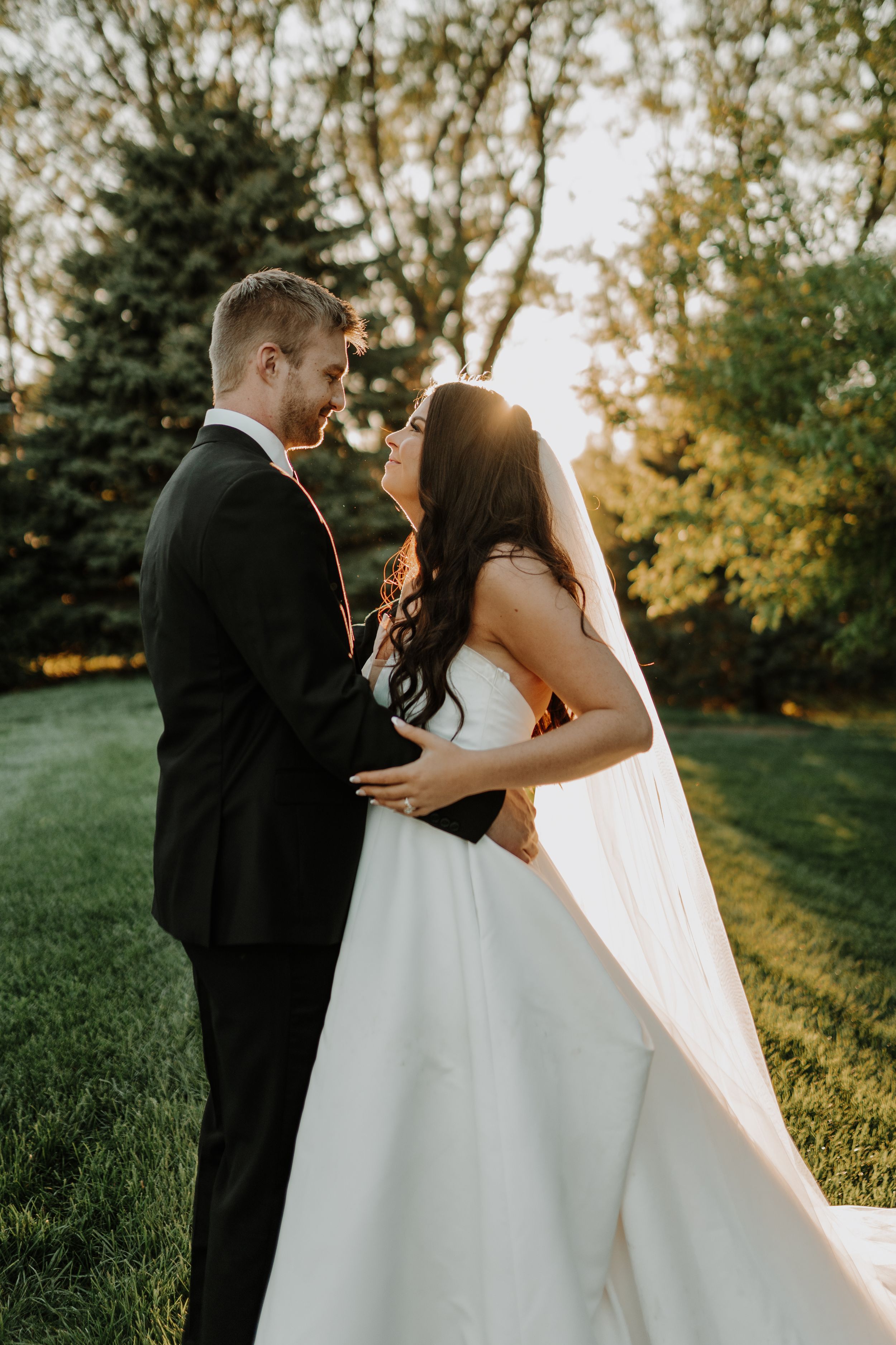 Intimate wedding portrait of couple embracing in a garden setting during sunset.