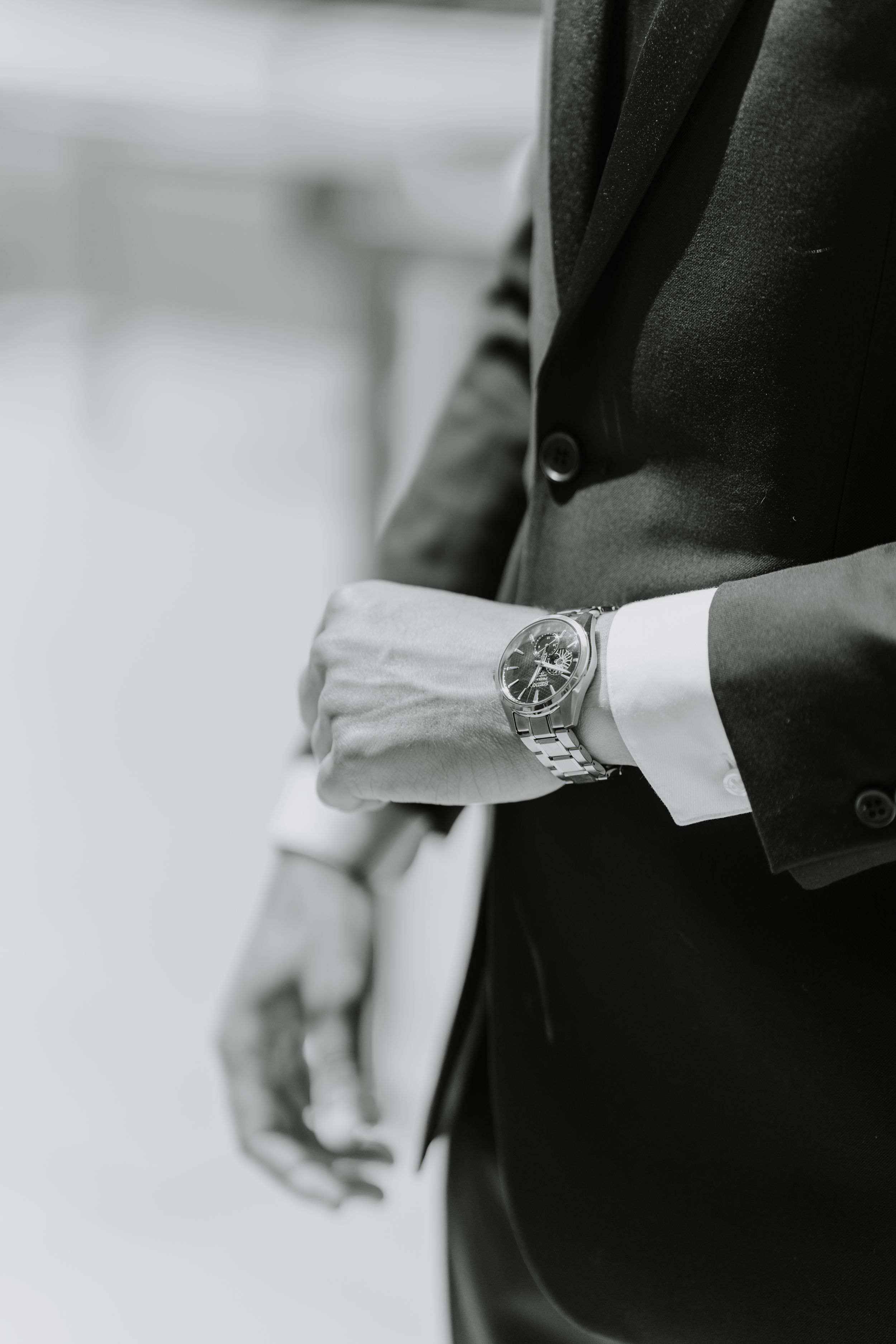 Close-up black and white photo of a metallic watch on a suited wrist.