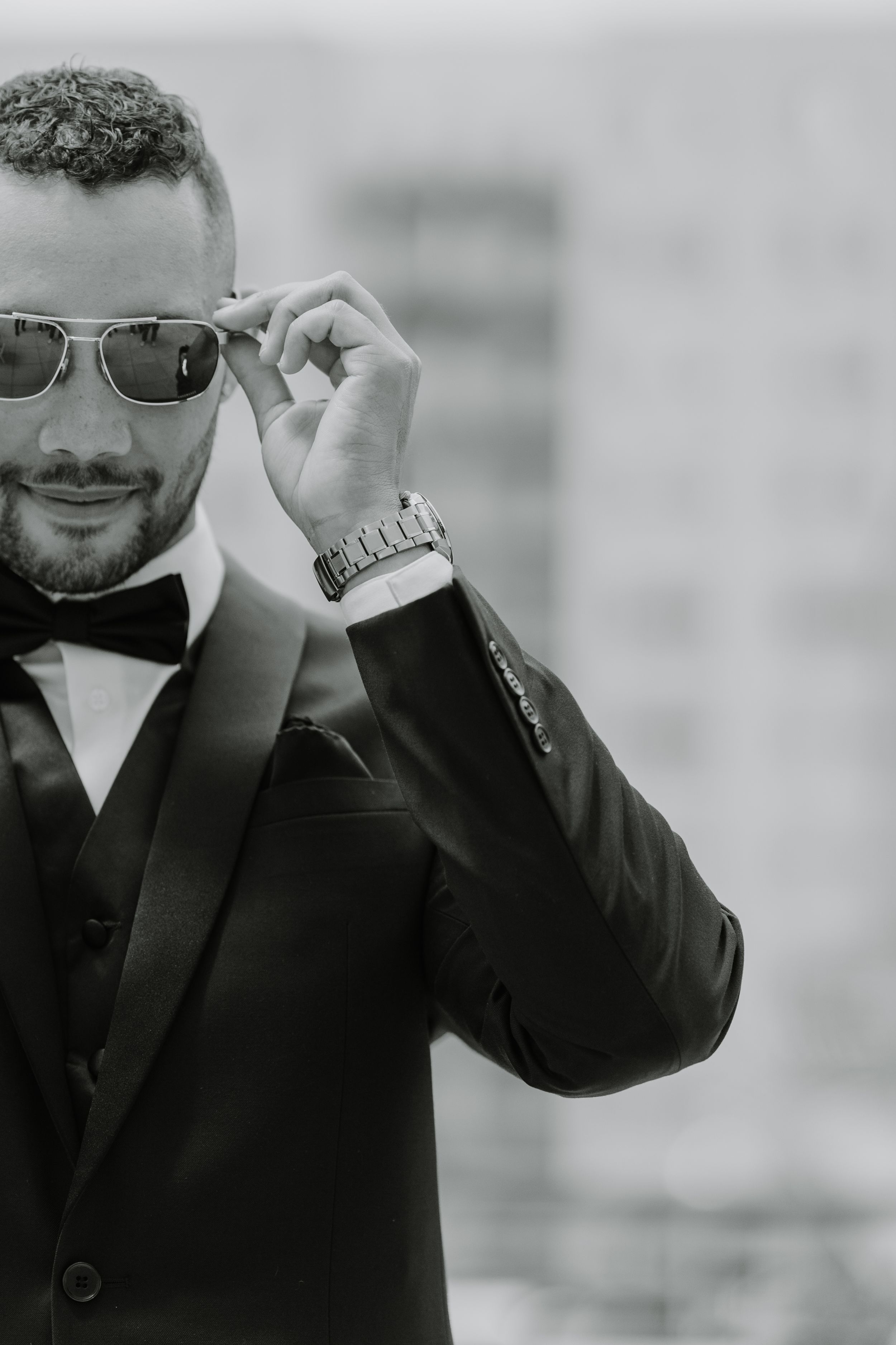 Black and white portrait of a suited person adjusting sunglasses.
