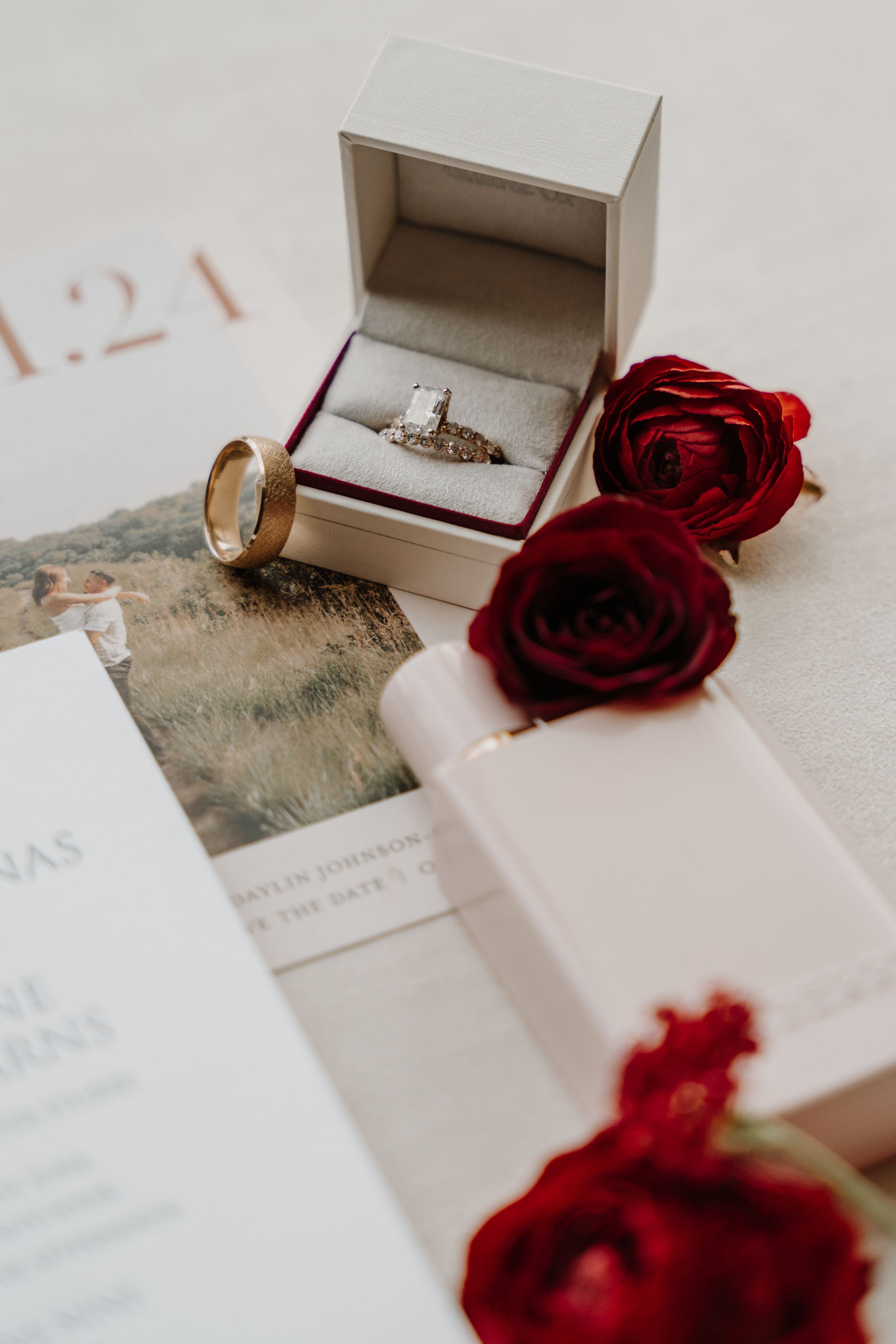Engagement ring in white box with red roses and wedding stationery.