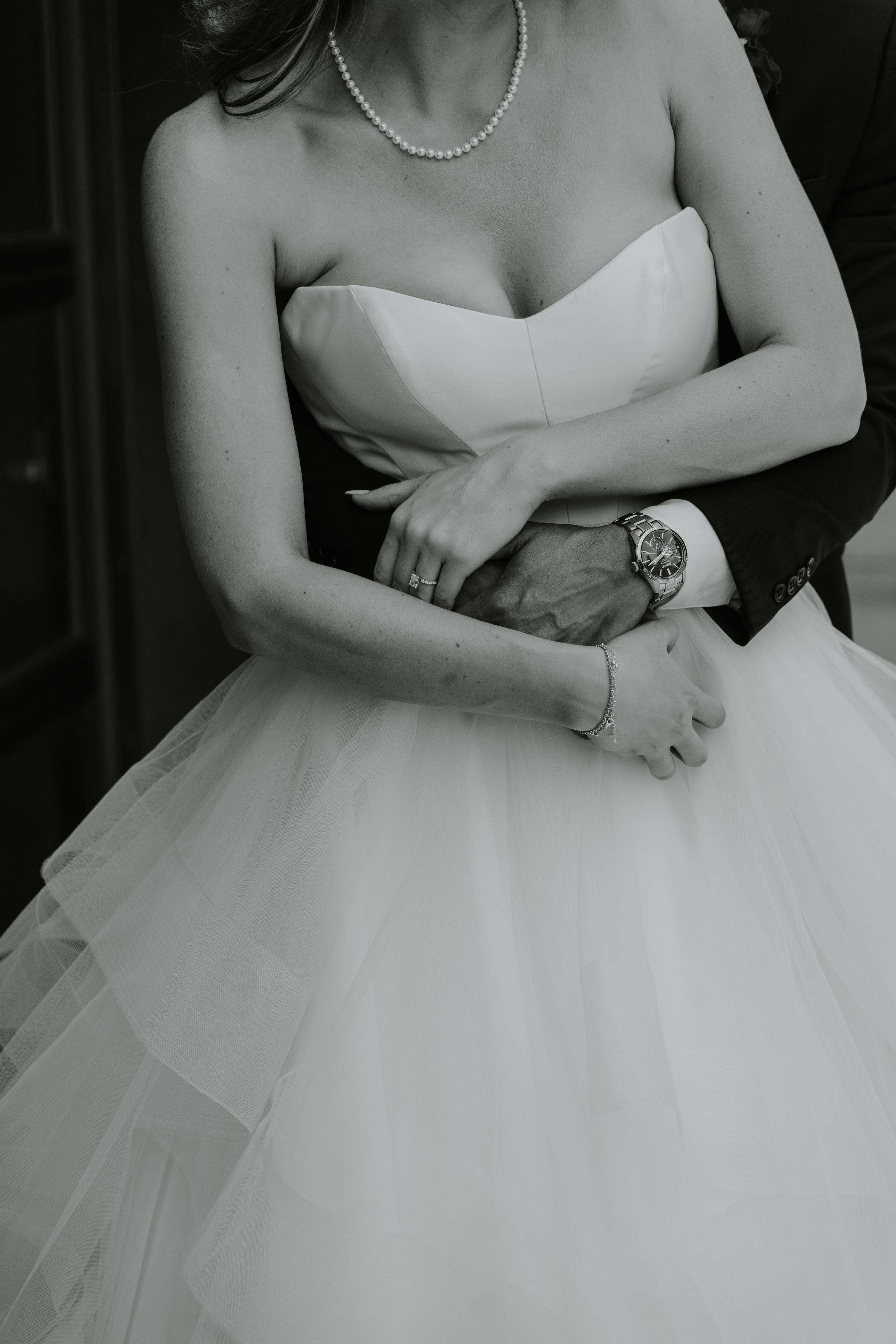 Close-up details of a bride's elegant white strapless wedding dress and pearl necklace.