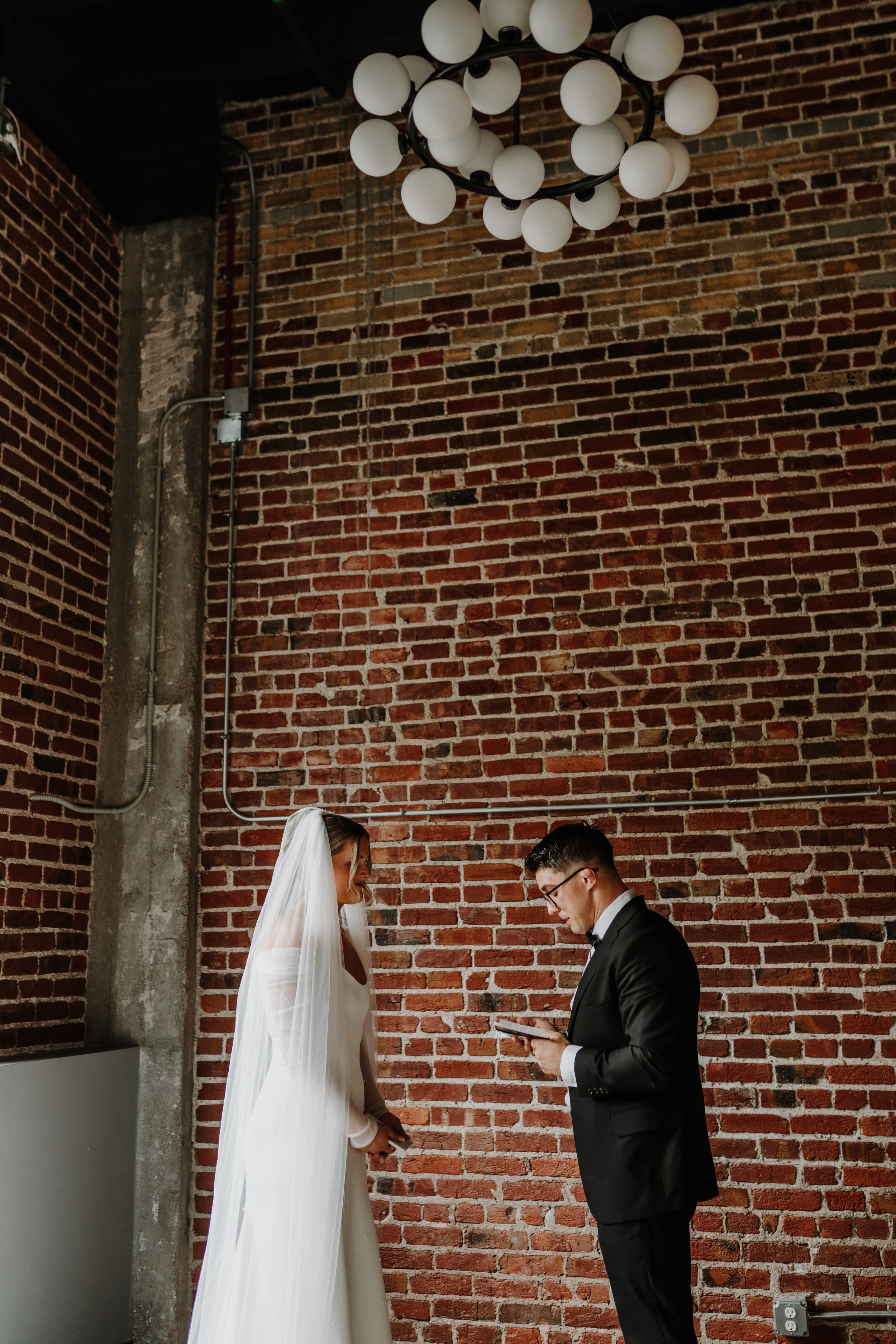 Wedding couple standing against rustic brick wall with modern white balloon installation.