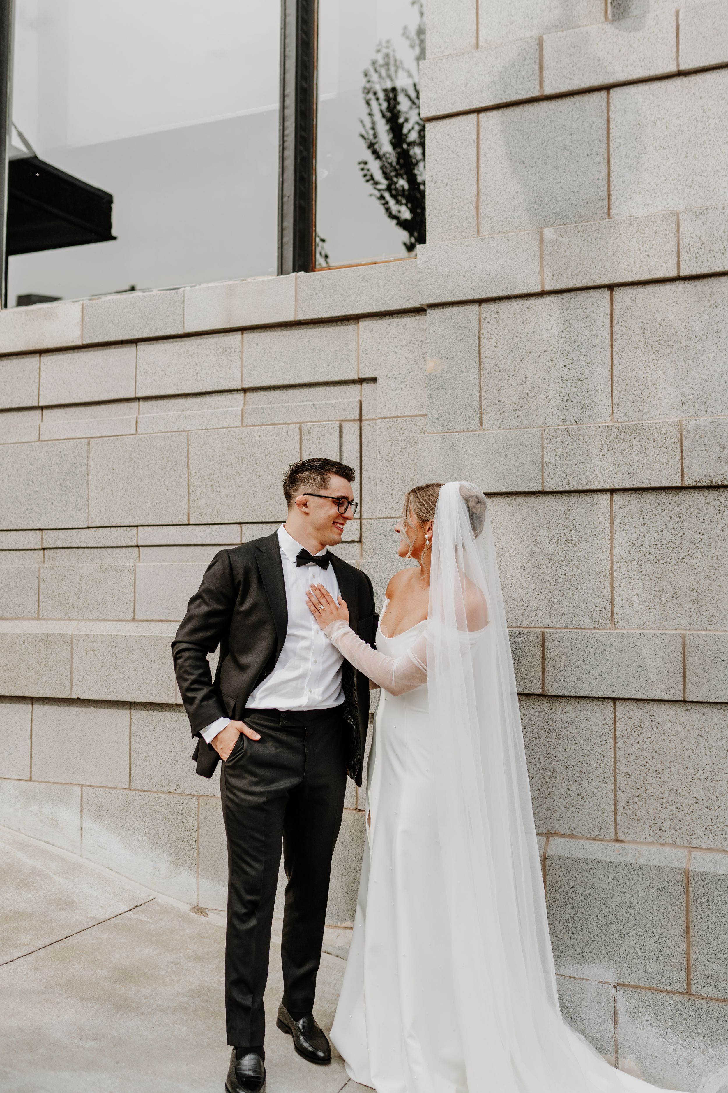 Candid portrait of wedding couple sharing tender moment against stone architecture.