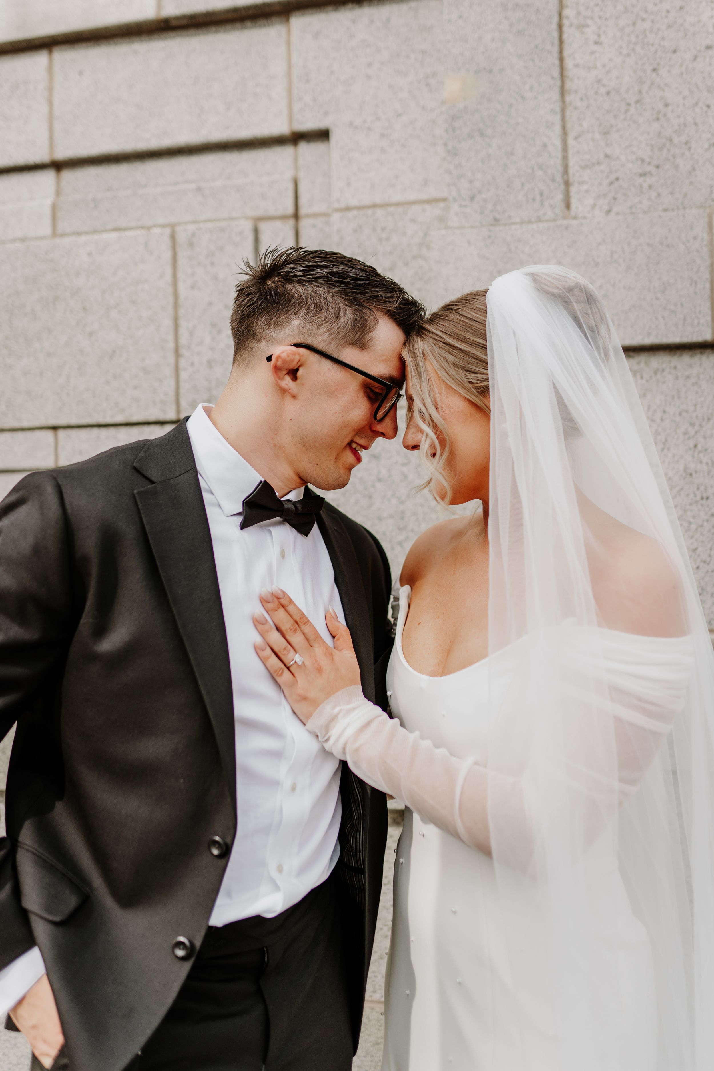 Intimate moment between bride and groom against stone wall backdrop.