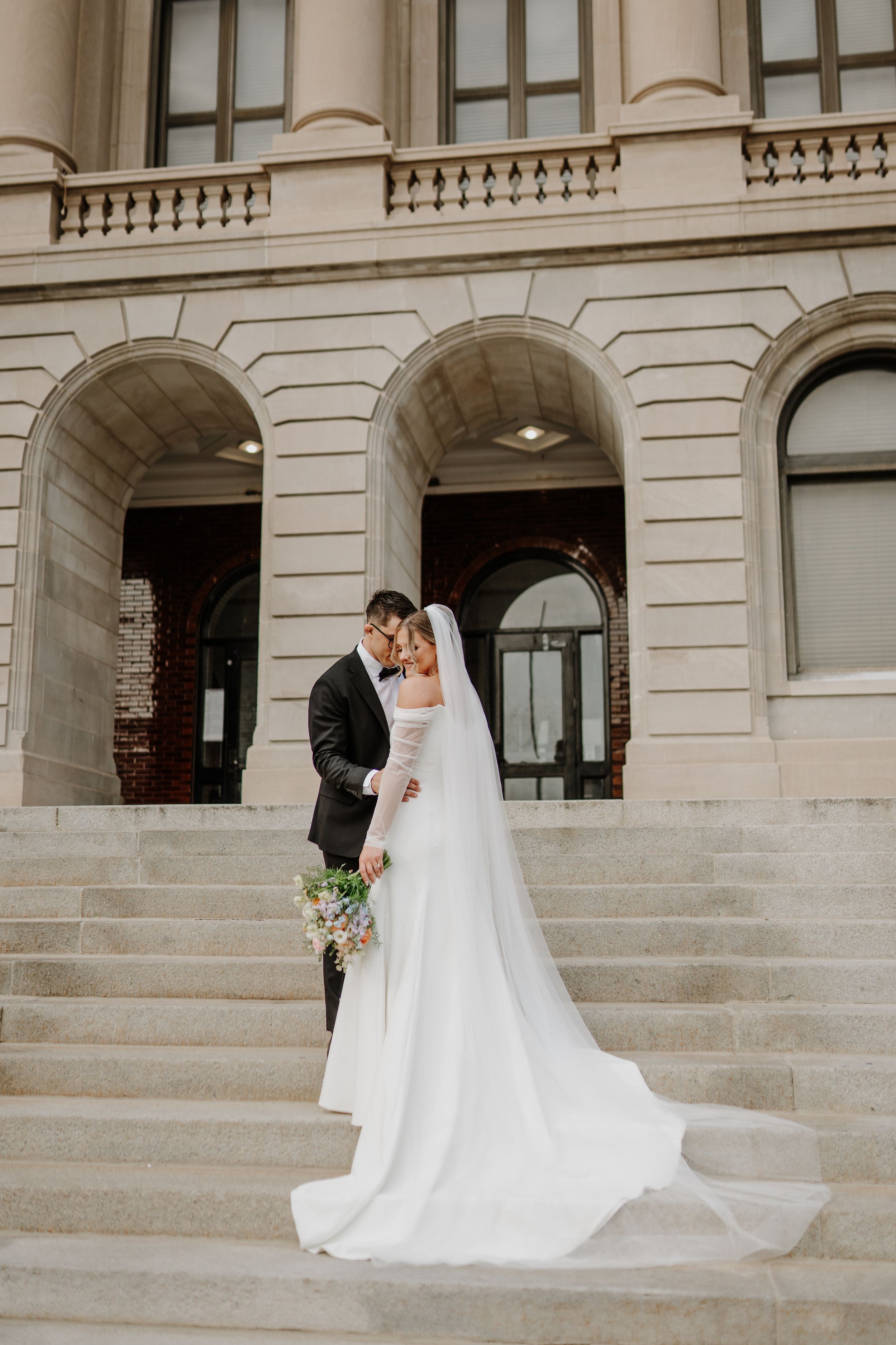 Elegant wedding photo of couple standing on marble steps of historic building.