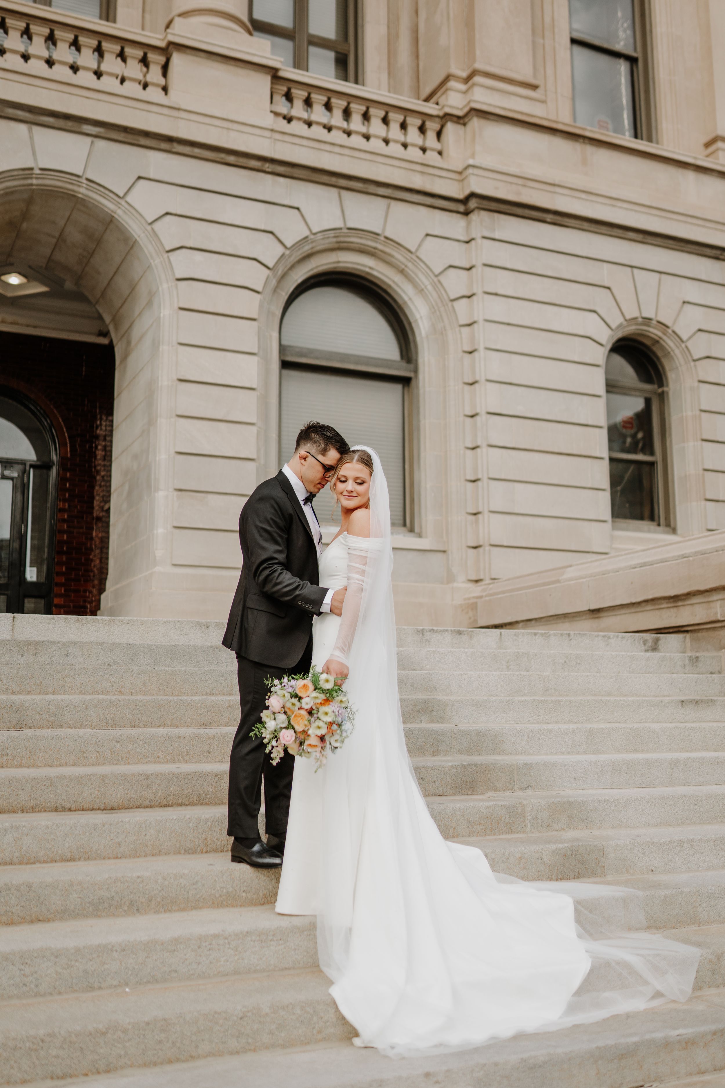Romantic wedding portrait captured on grand stone staircase of historic building.