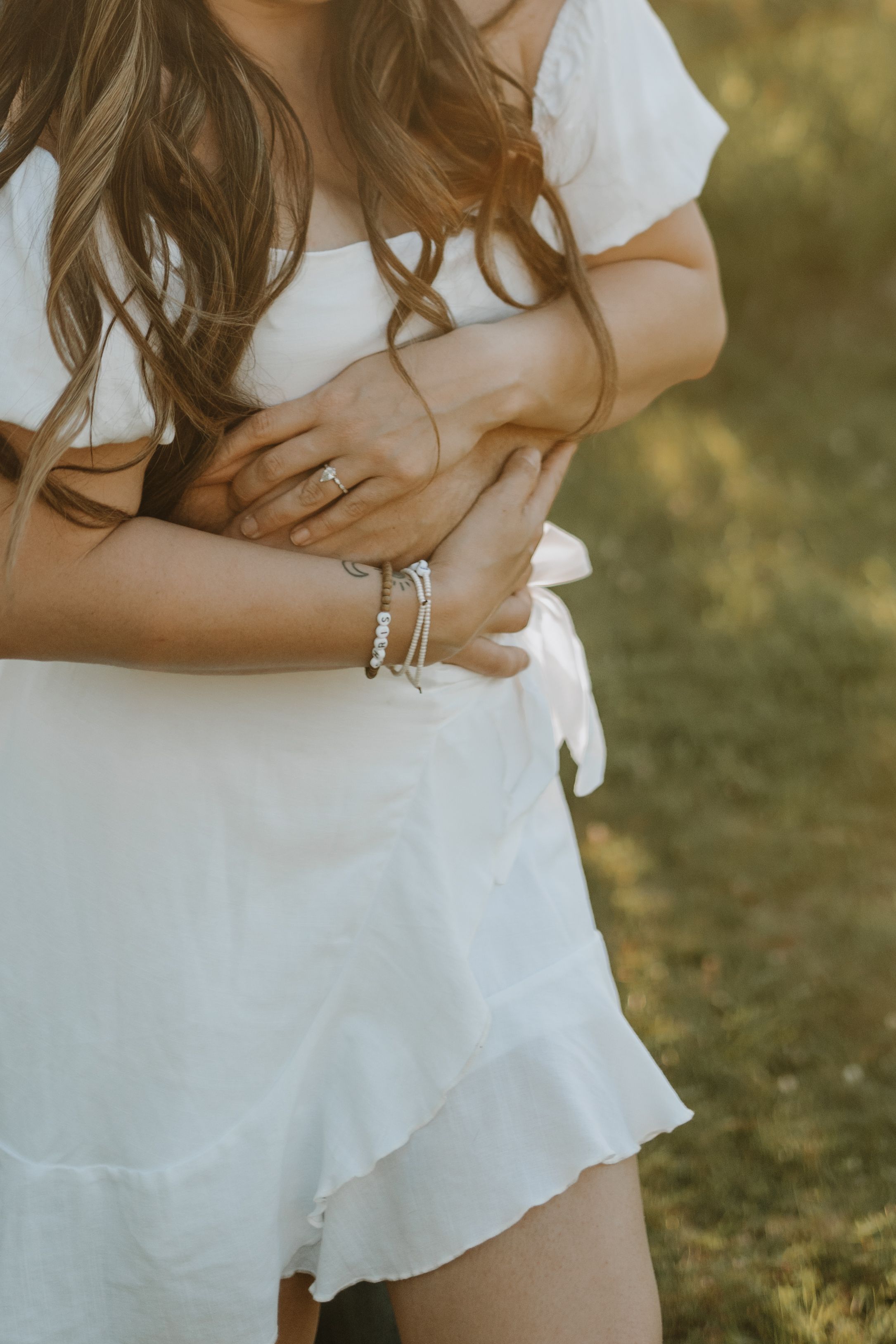 Woman in white dress shows silver bracelets against sunlit outdoor backdrop.