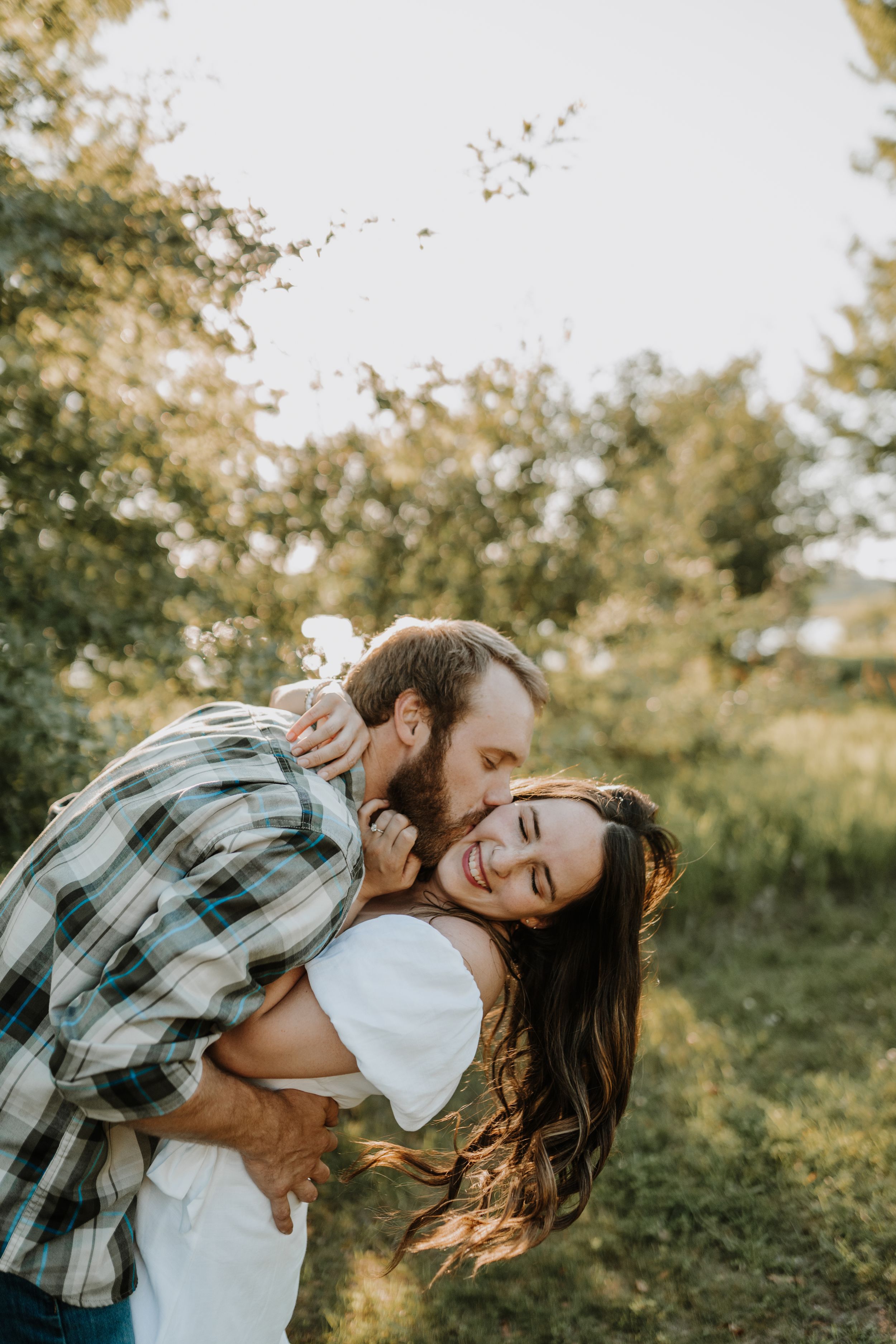 Playful couple laughing during outdoor photoshoot in golden sunlight.