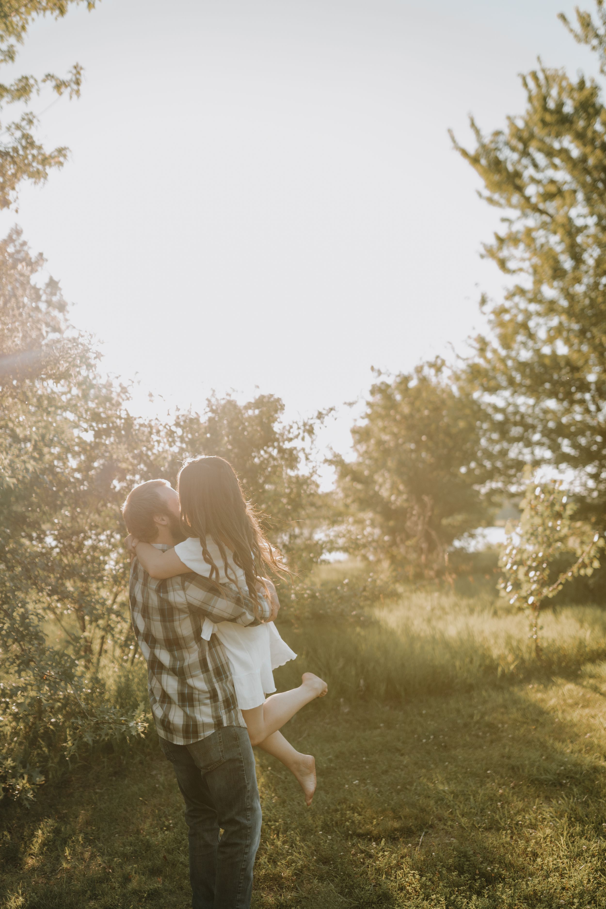 Man lifts woman in white dress during romantic outdoor photoshoot.