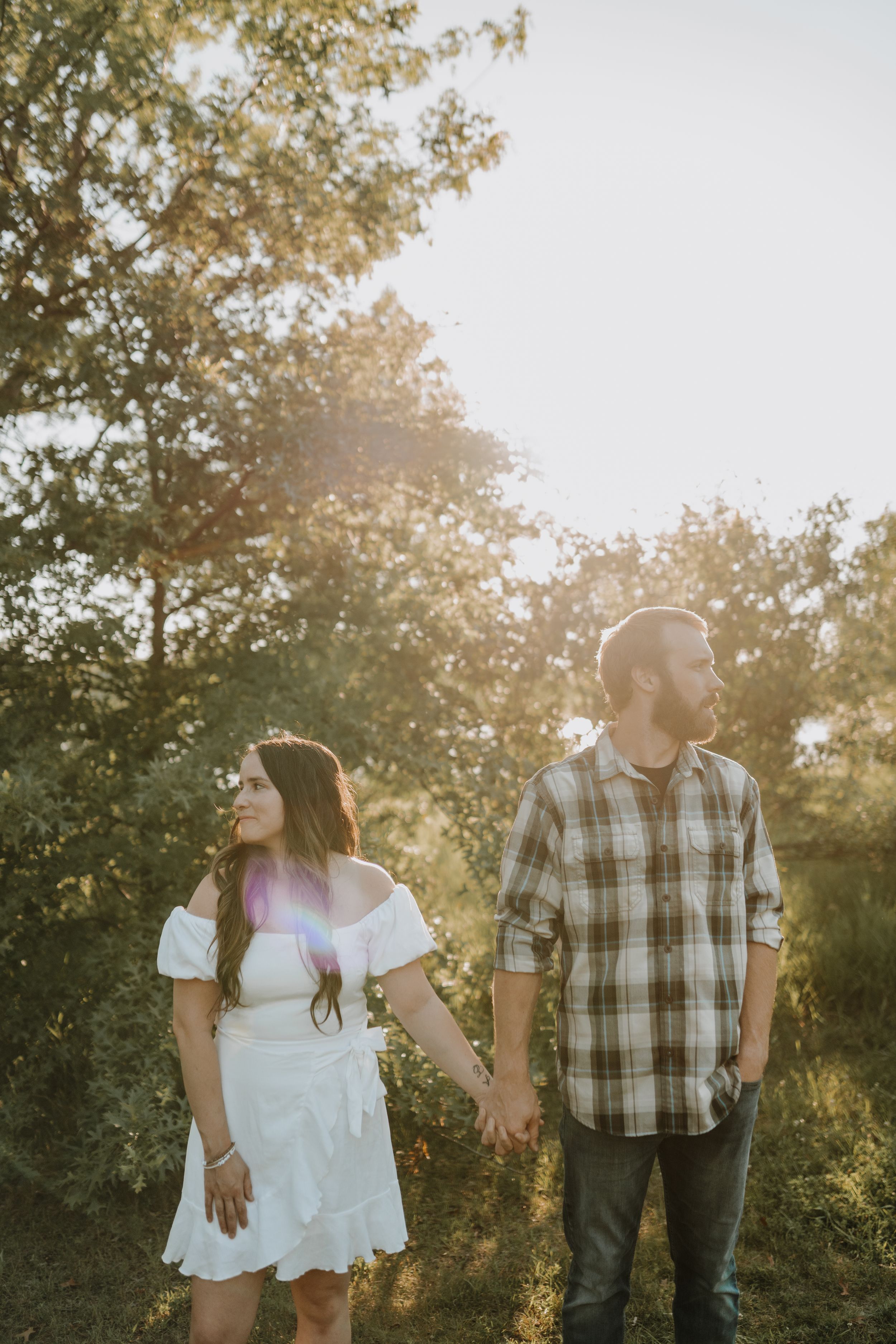 Couple holding hands while walking through sunlit meadow at golden hour.