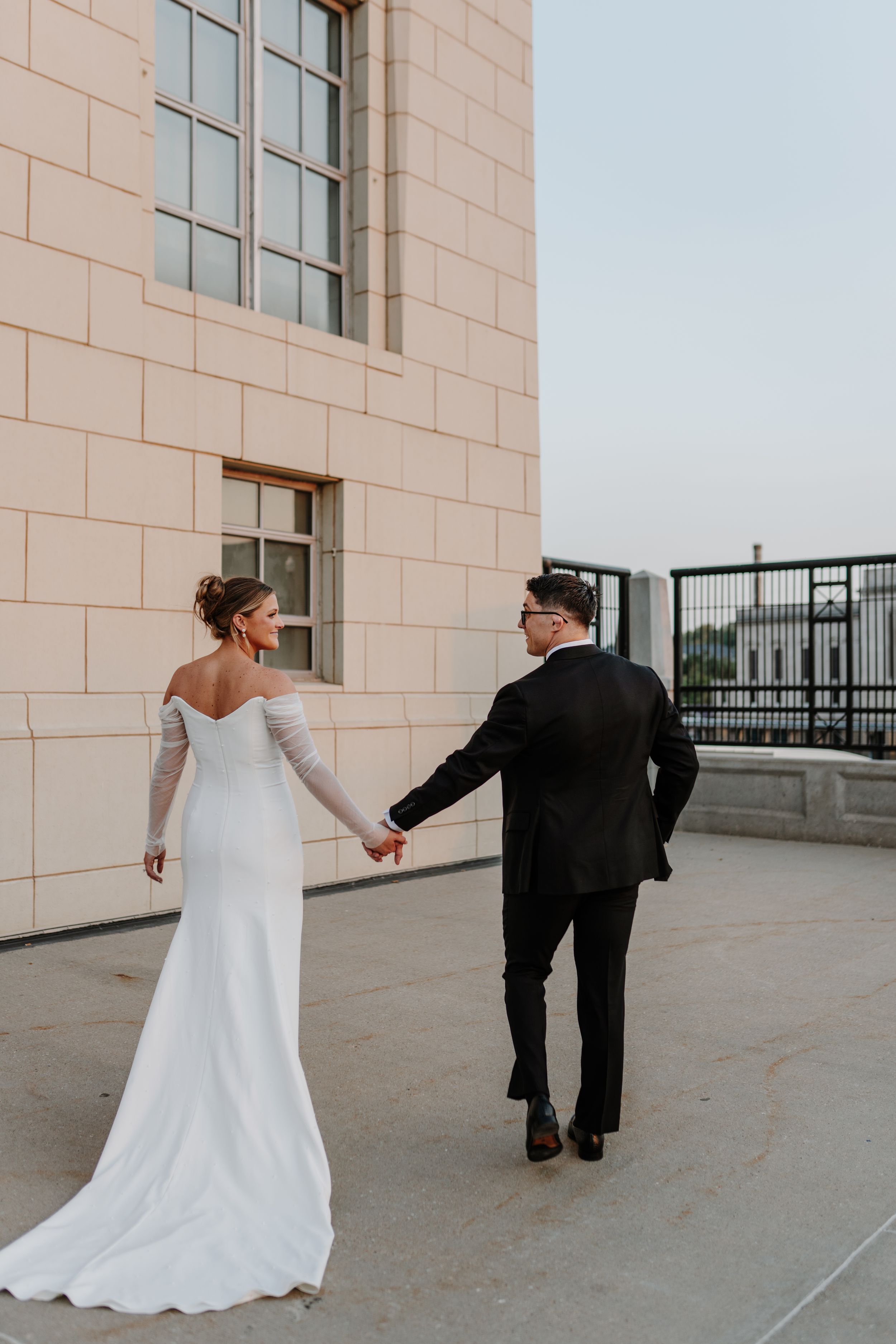 A newlywed couple walking together on a rooftop terrace in formal wedding attire.