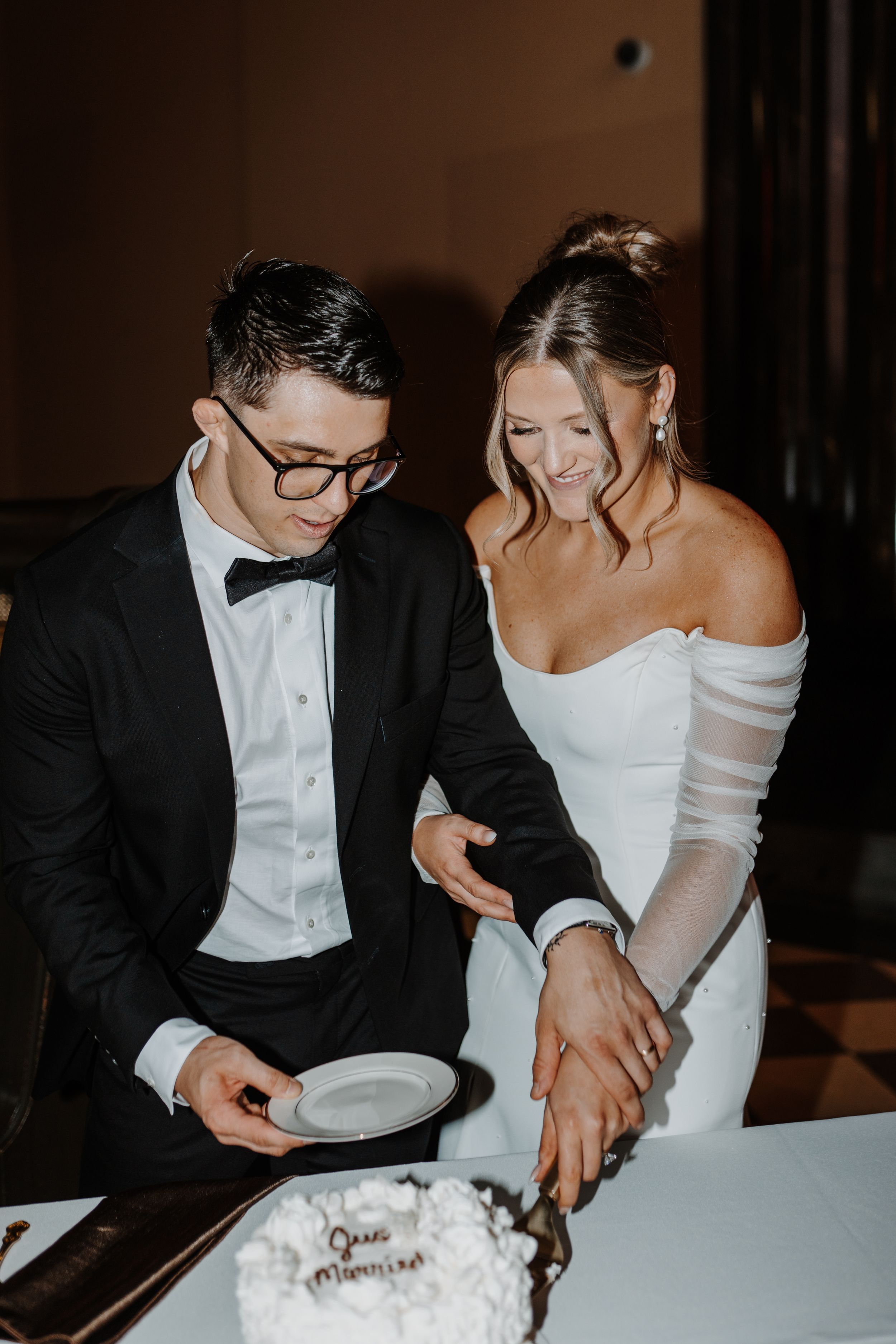 Couple cutting their white wedding cake together during reception celebrations.
