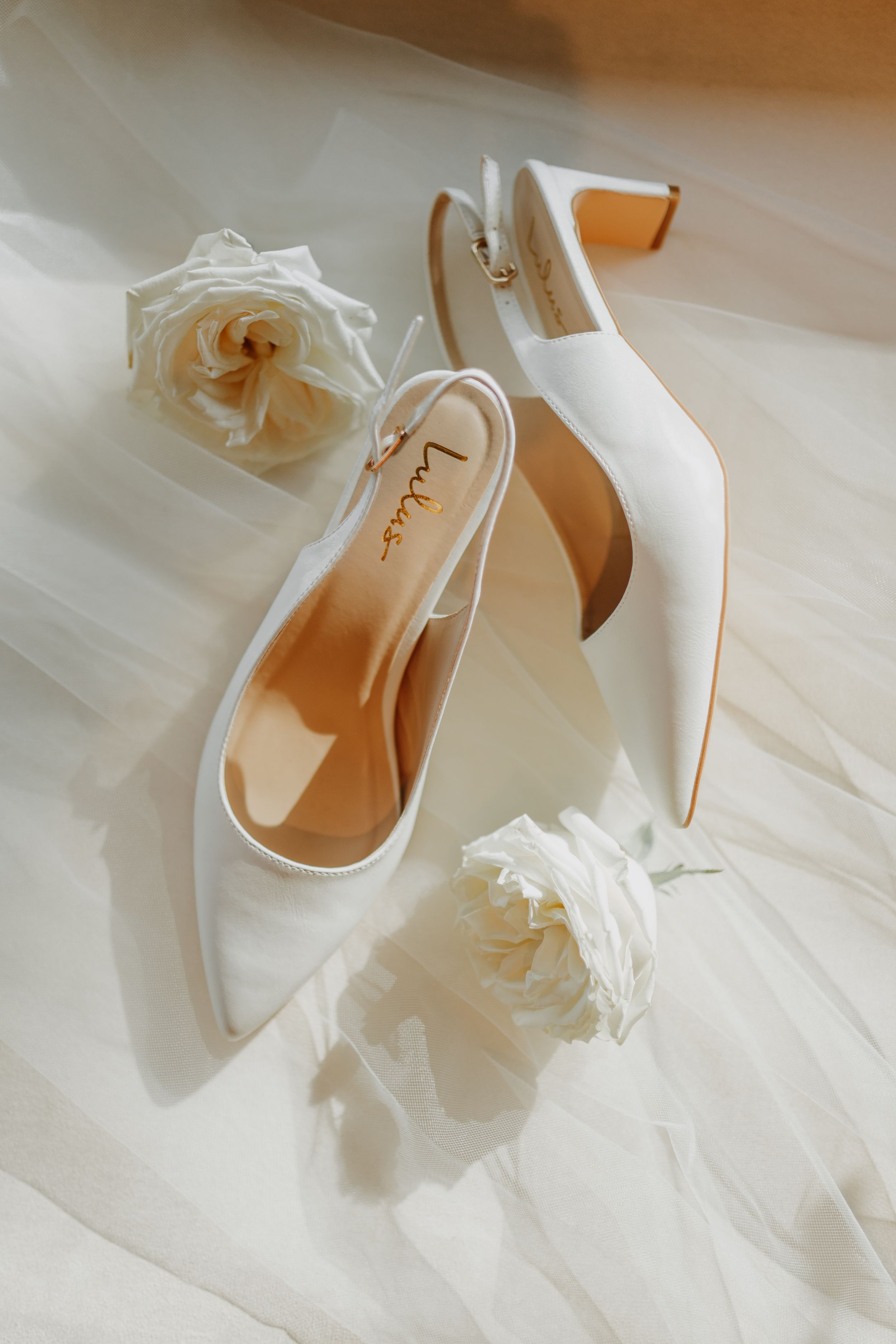 Elegant white bridal shoes with floral details on a light wooden floor.