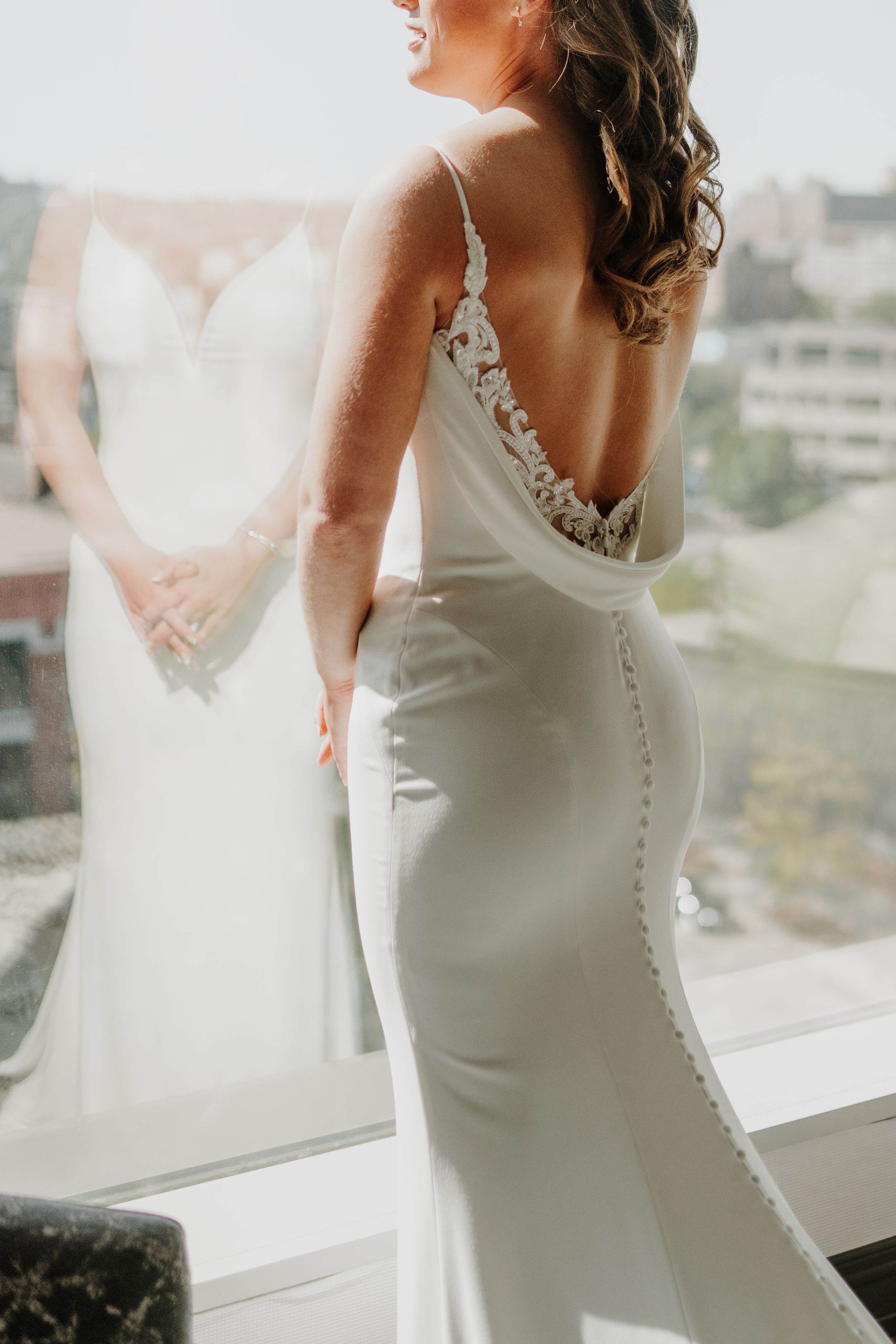 Elegant fitted wedding dress with button details photographed by a window.