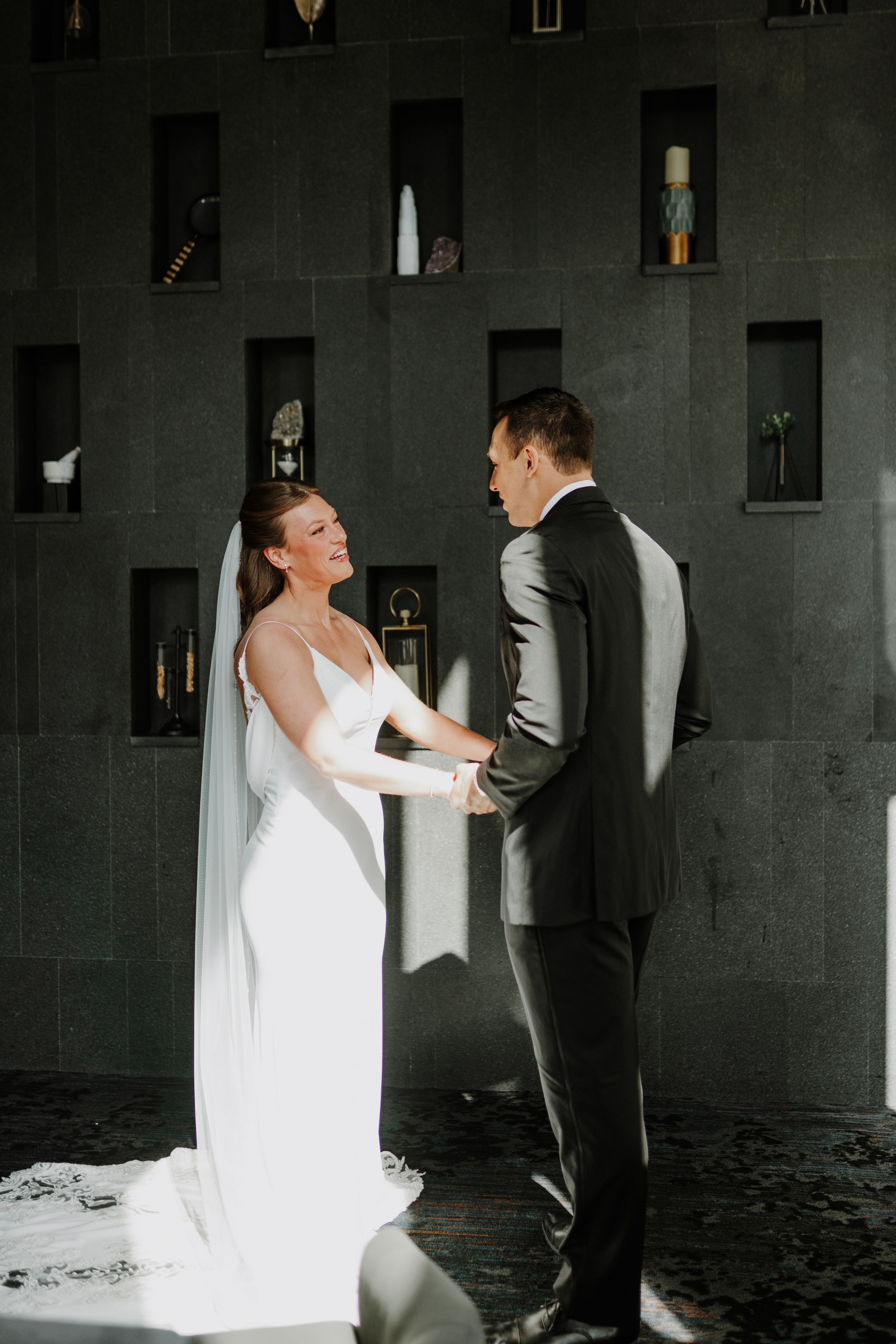 Dramatic first look wedding moment captured against dark textured wall.